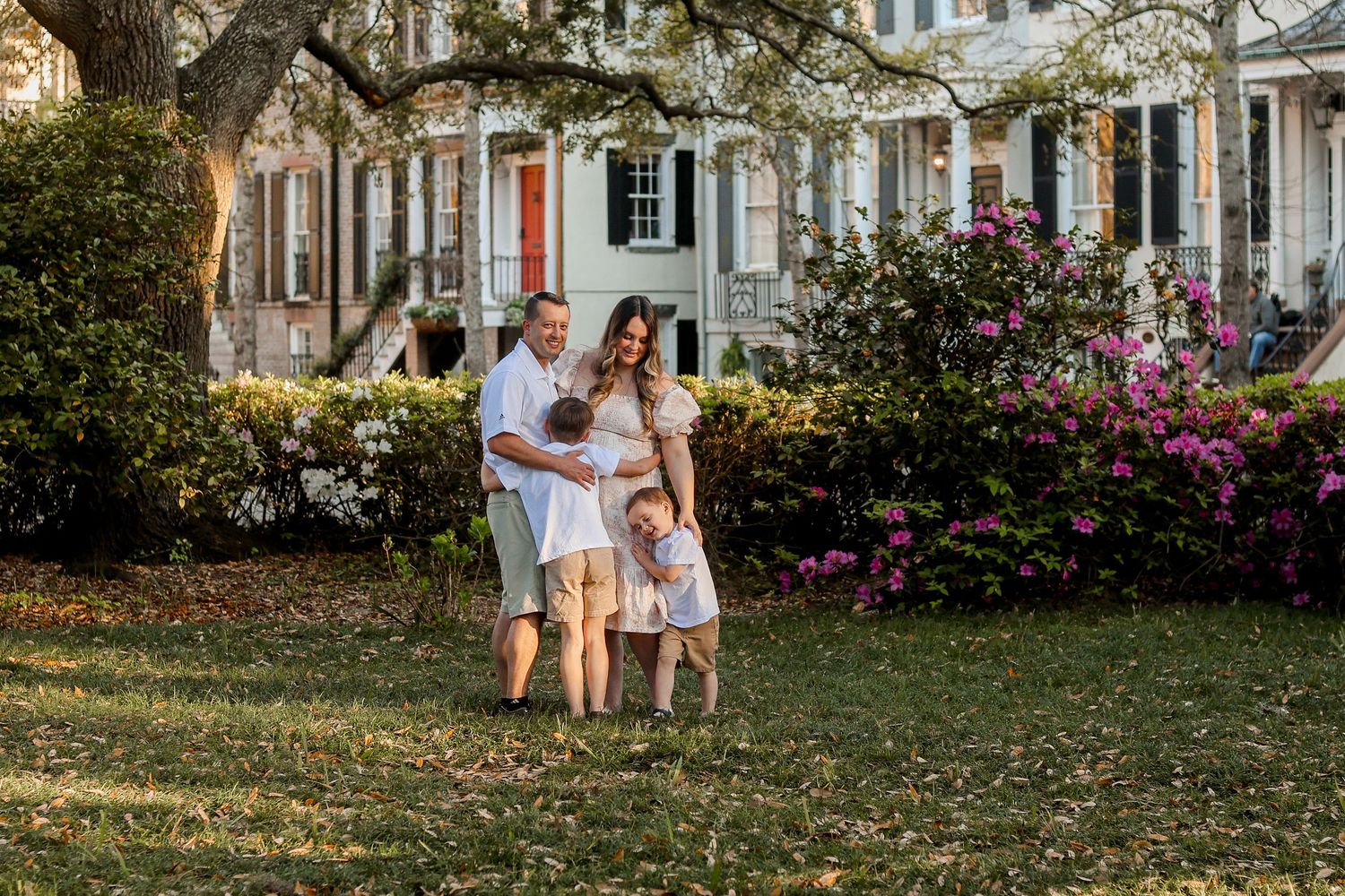 A family portrait taken on a lawn with blooming azaleas and historic architecture in background.