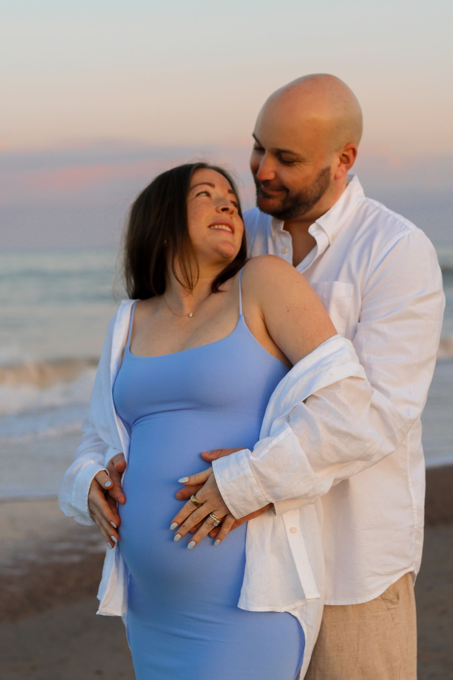 Tender beach maternity portrait with soft sunset lighting.