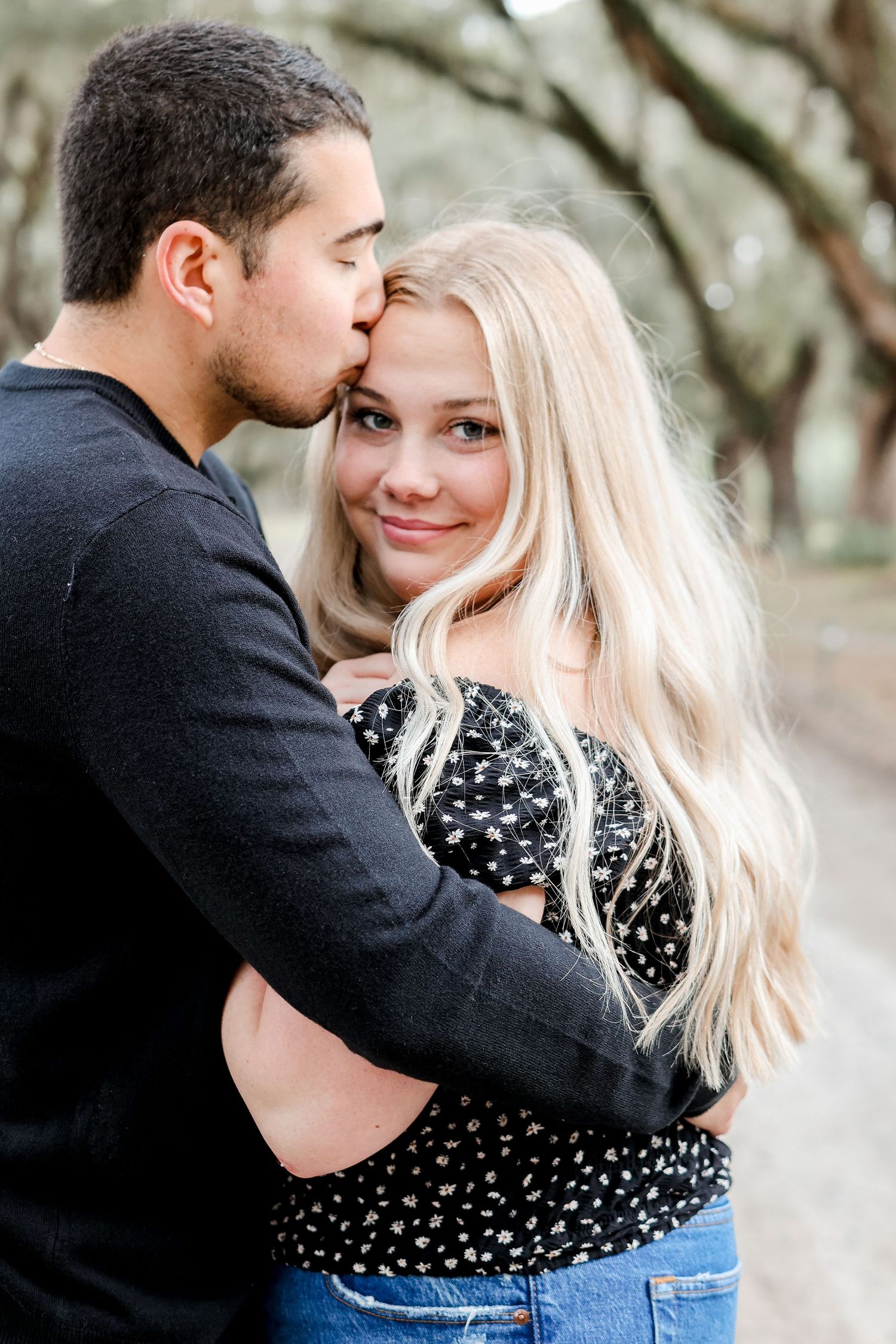 Romantic couple embracing in black and polka dot clothing against a natural backdrop.