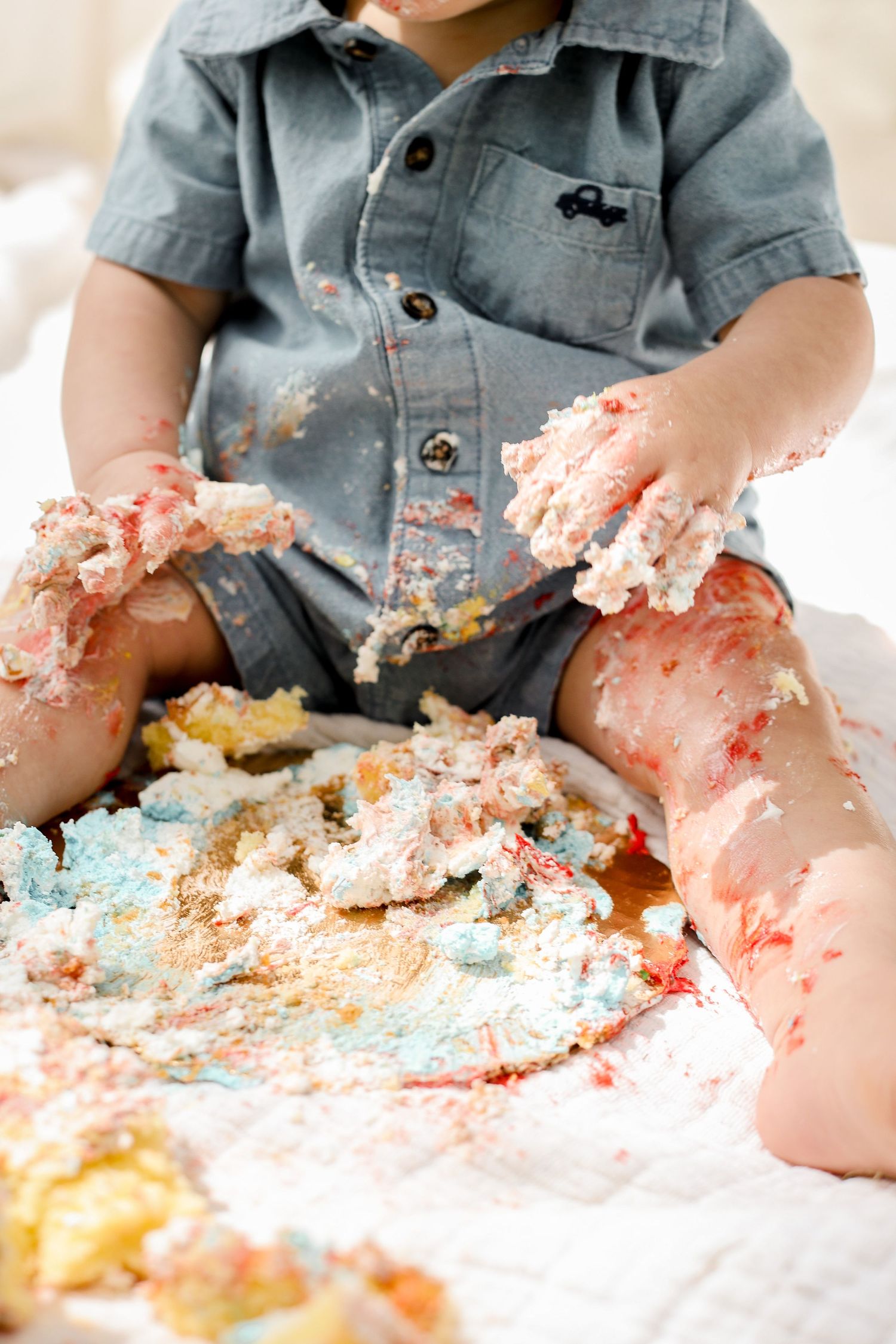 Close-up of messy cake smash with frosting-covered hands and denim outfit.