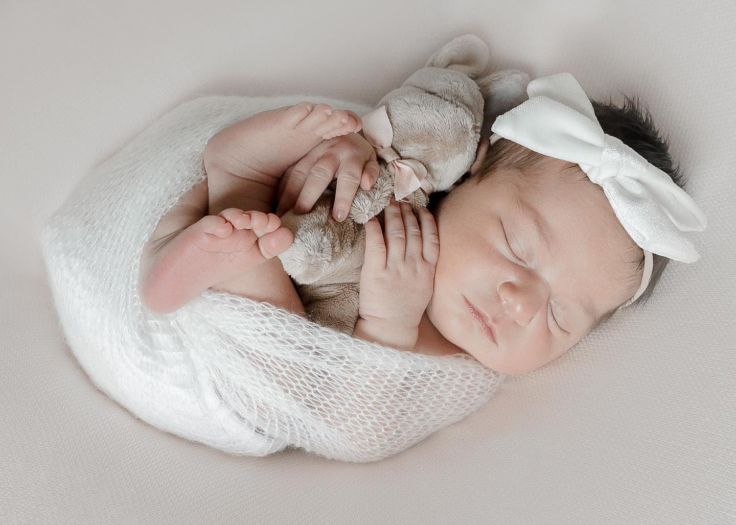 Newborn baby sleeps peacefully wrapped in white textured fabric.