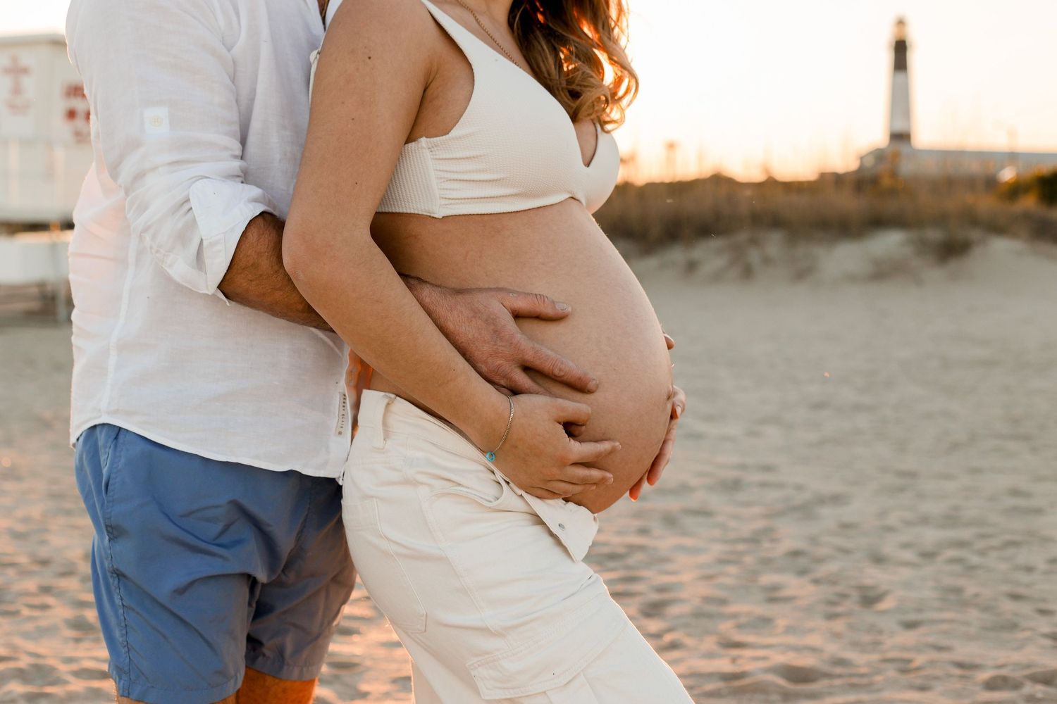 Happy family on a beach at sunset celebrating a pregnancy announcement with ultrasound photos.