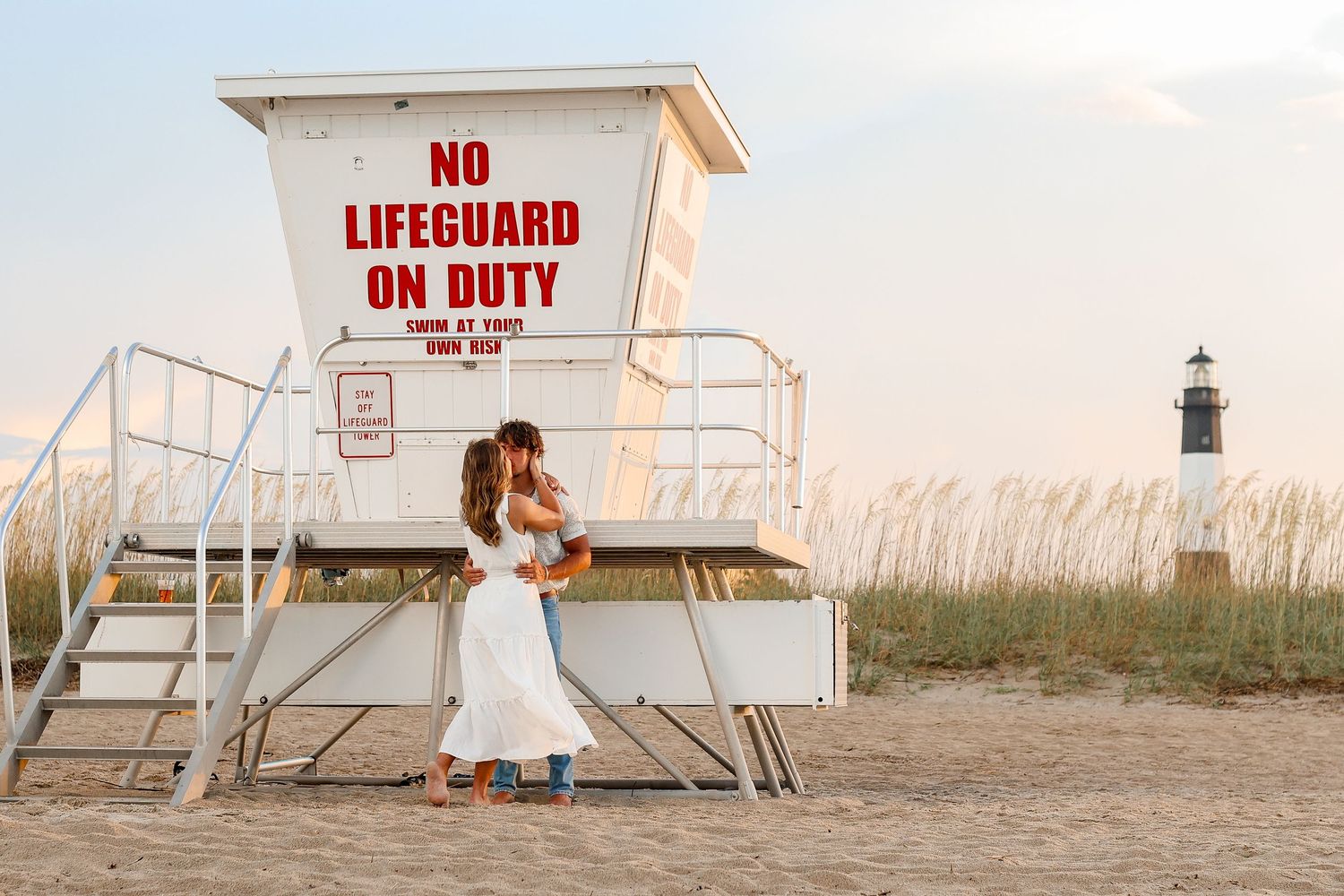 Romantic couple posing in front of a white lifeguard tower during sunset.
