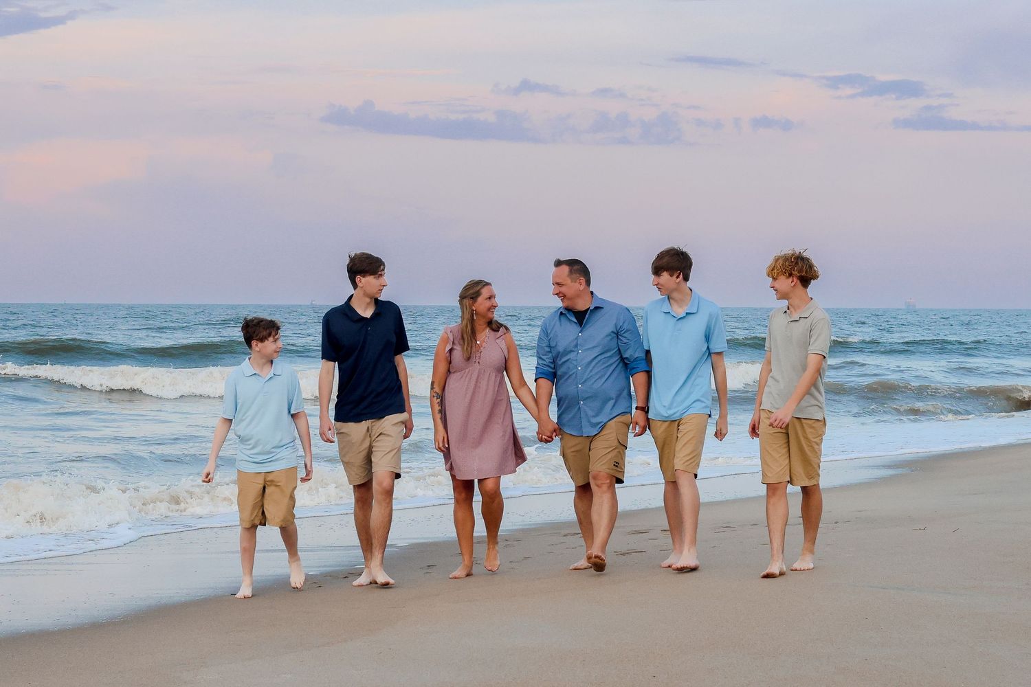 Family walking together along beach shoreline at sunset wearing coordinating casual attire.