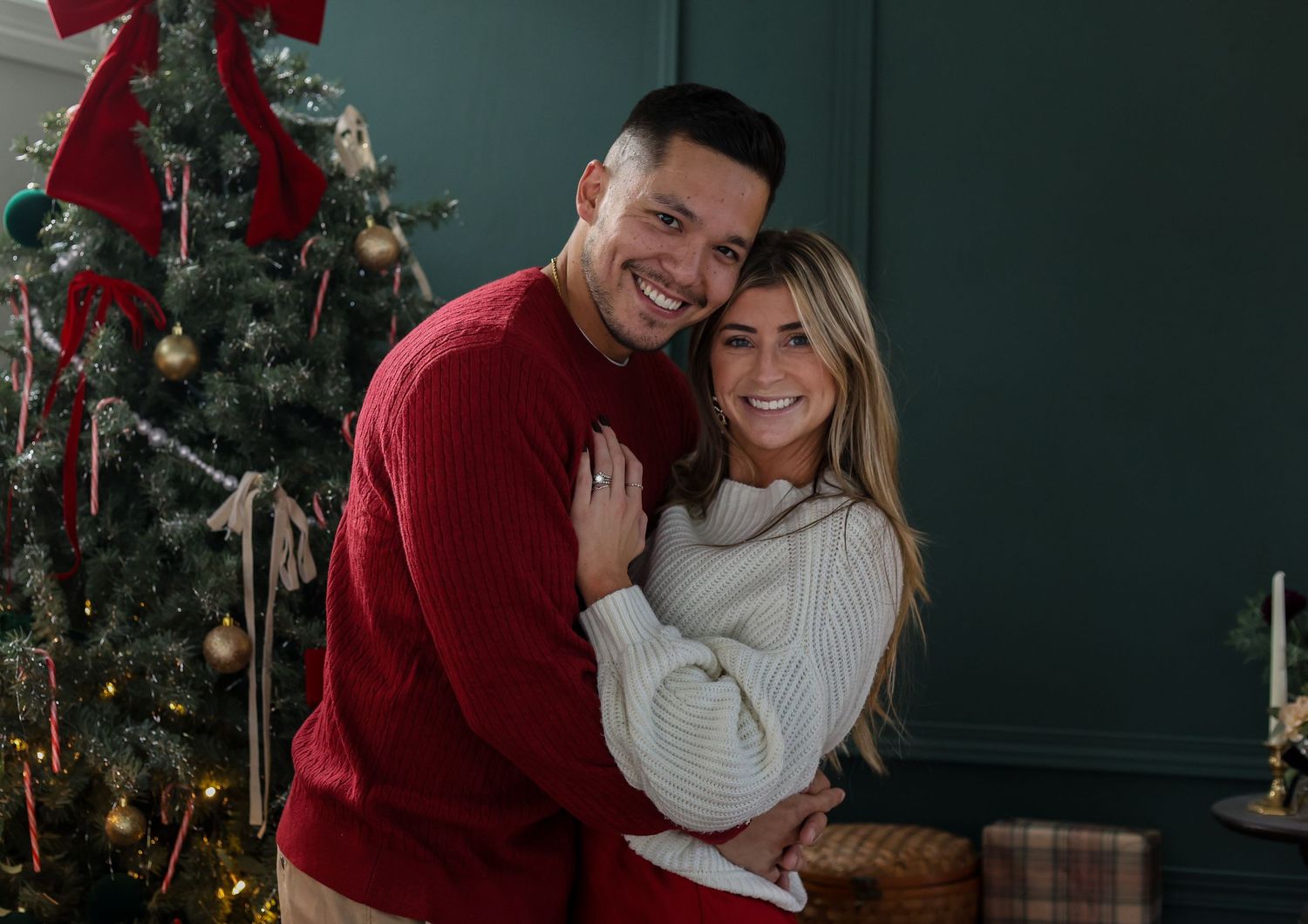 Couple sharing intimate moments by decorated Christmas tree in cozy dark green room with holiday ambiance.