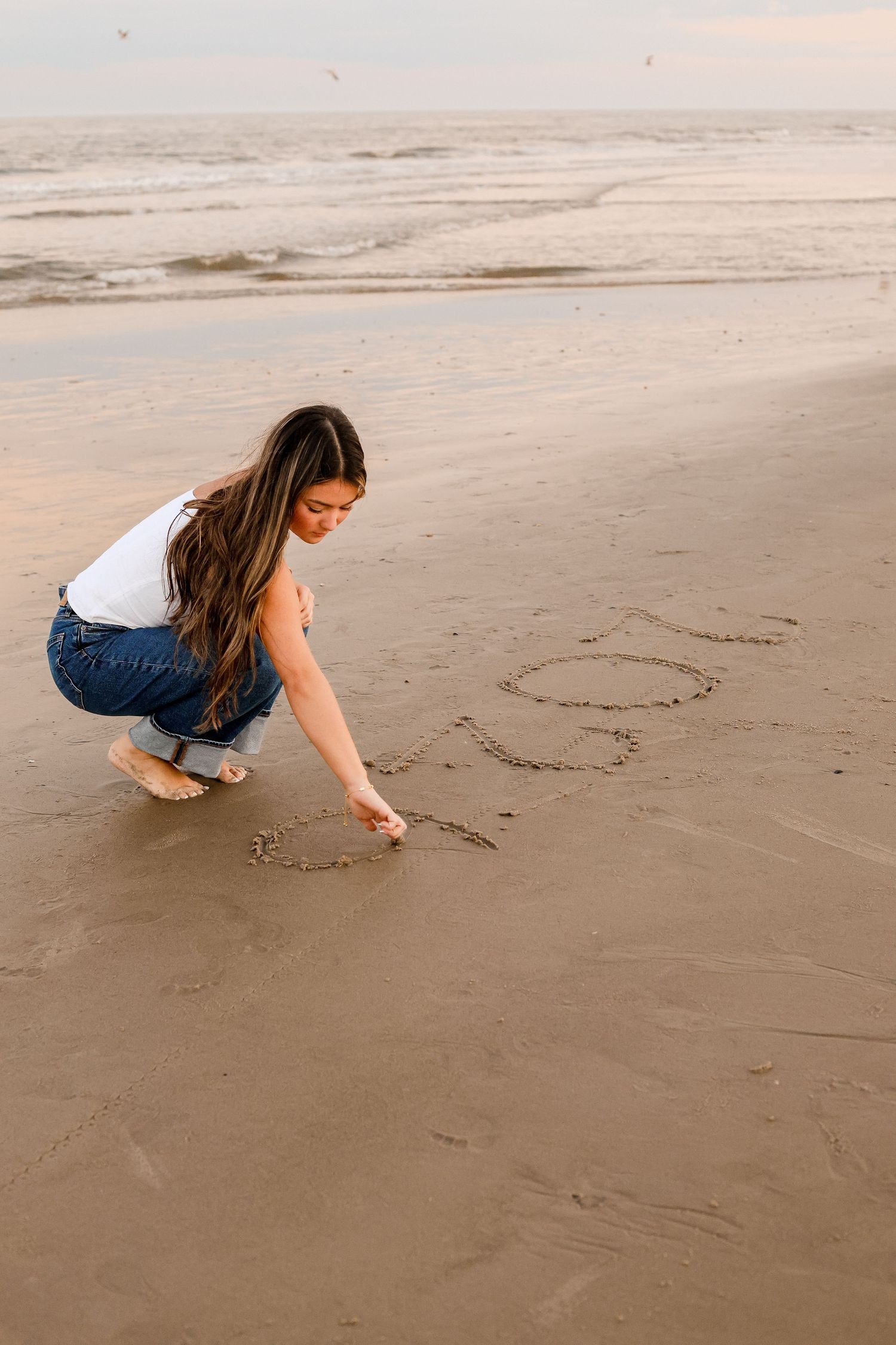 Someone drawing hearts in the sand on a serene beach during sunset.