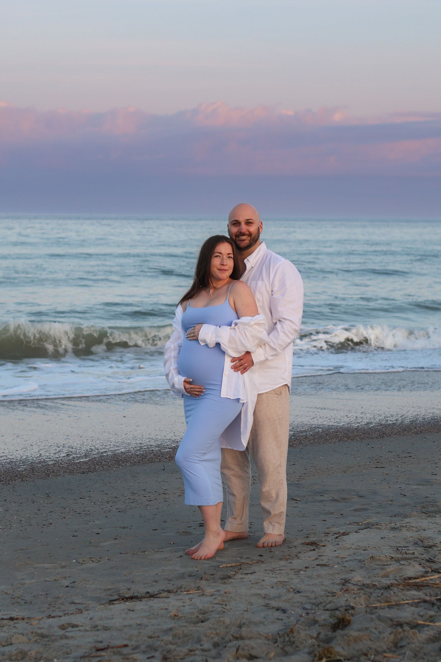 Sunset beach maternity photoshoot with ocean waves in the background.