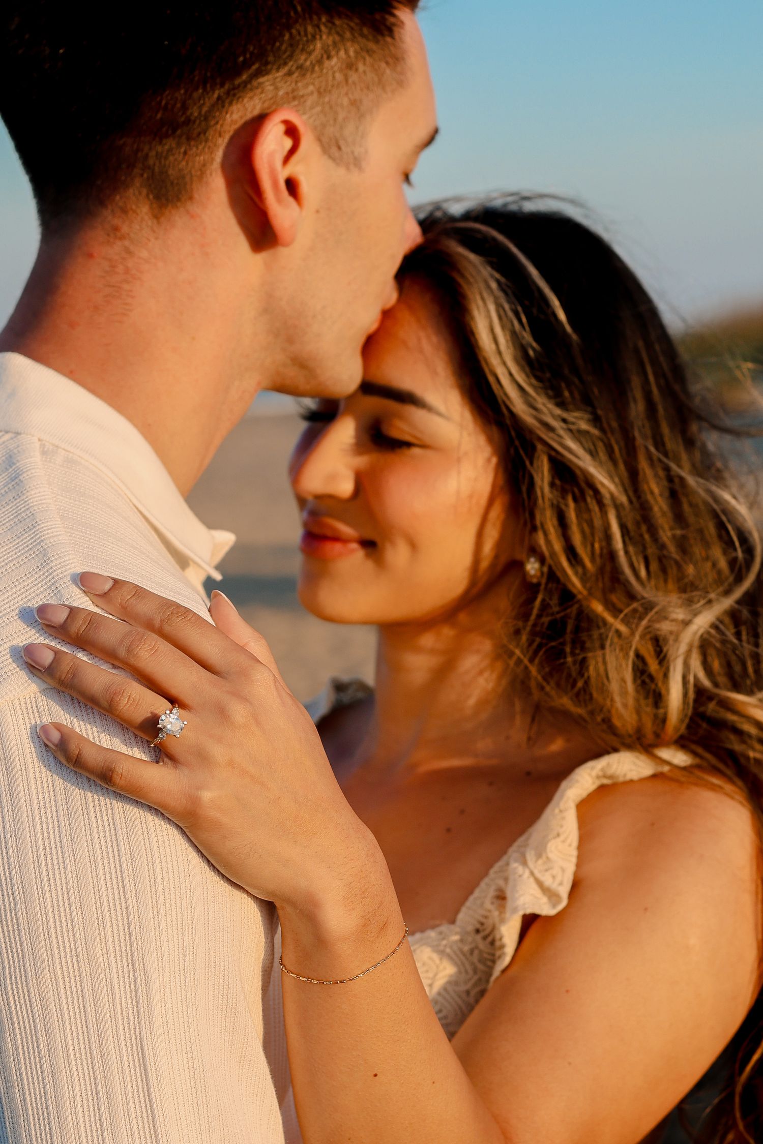 Close-up of engagement ring sparkles during intimate beach sunset moment.