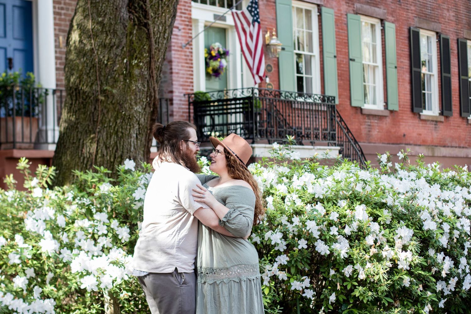 White azalea flowers bloom in front of a historic brick building with teal shutters.