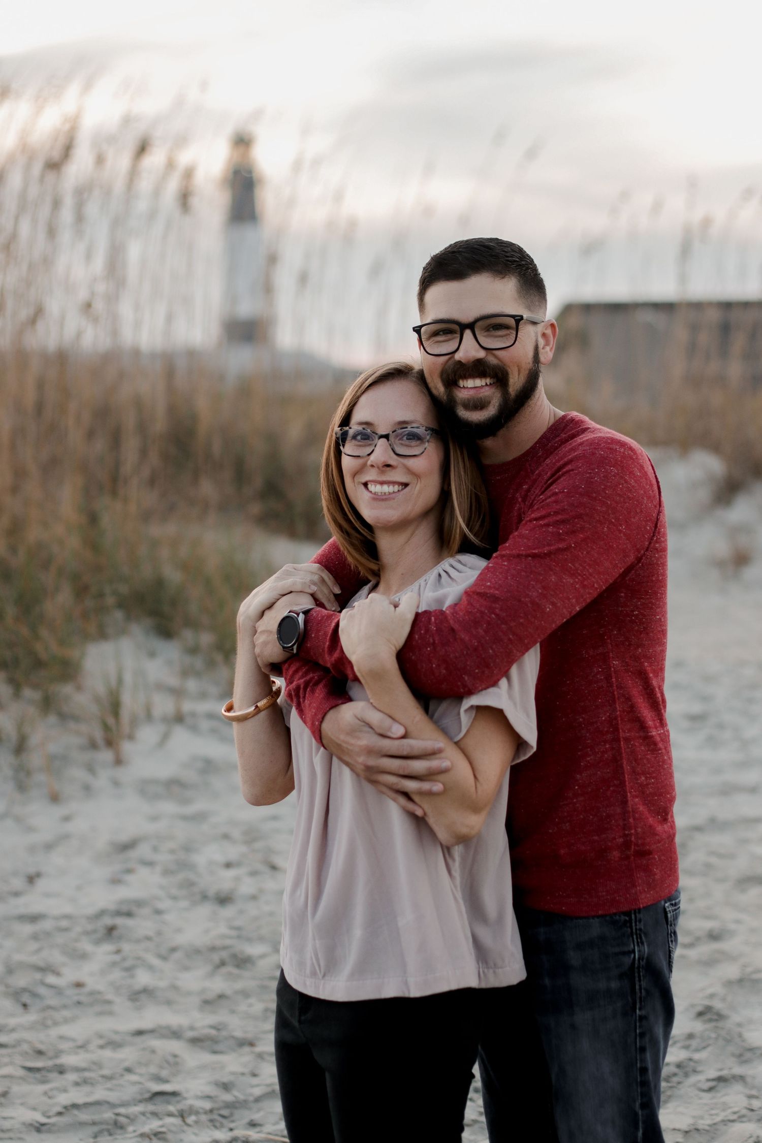 A couple shares a playful moment together on a beach with sand dunes in the background.