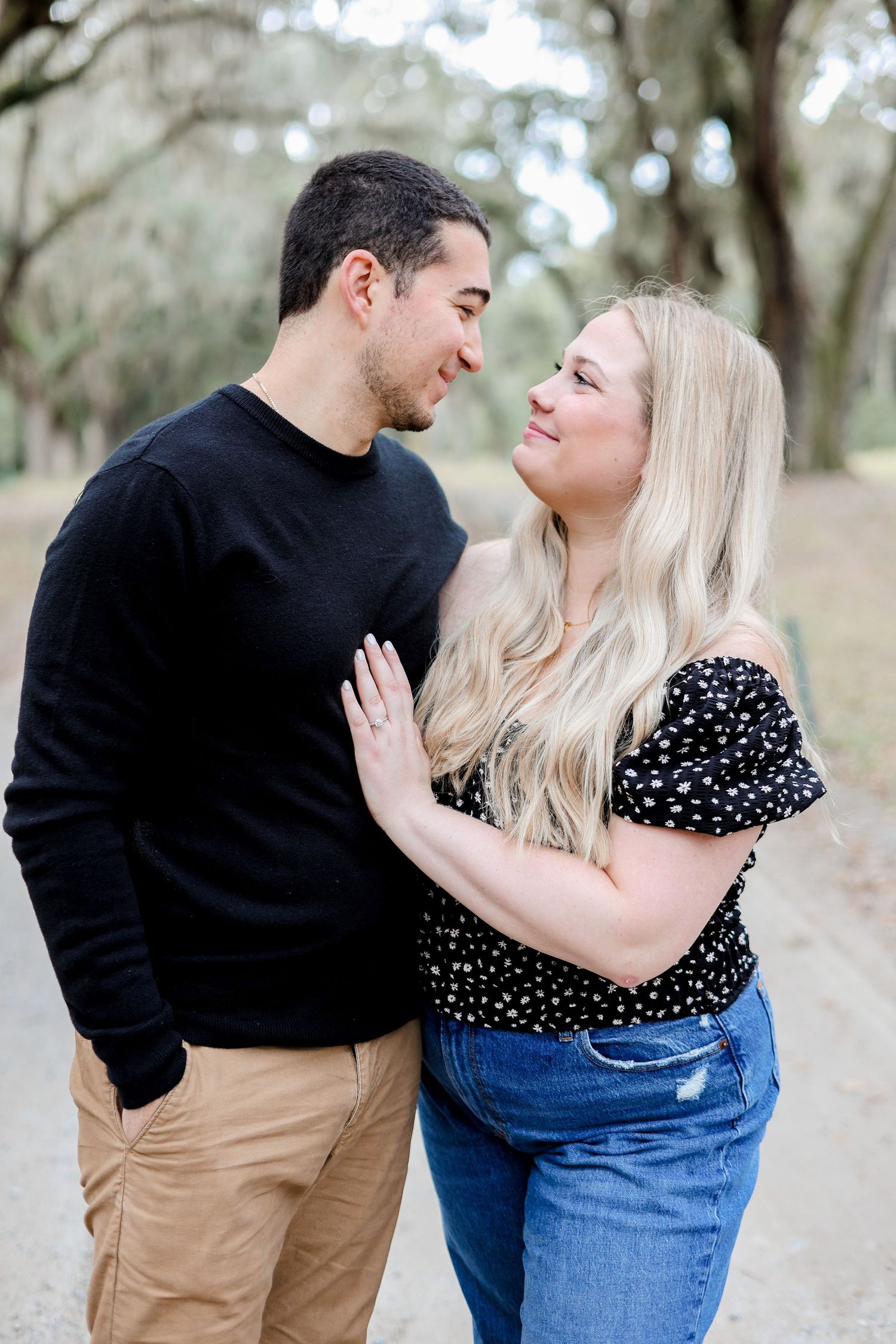 Romantic couple in casual wear sharing intimate moments along a tree-lined path.