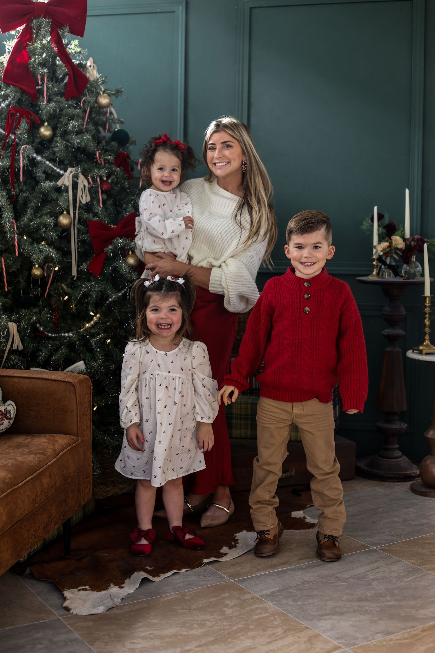 A festive holiday family portrait in front of a decorated Christmas tree with coordinated red and white outfits.