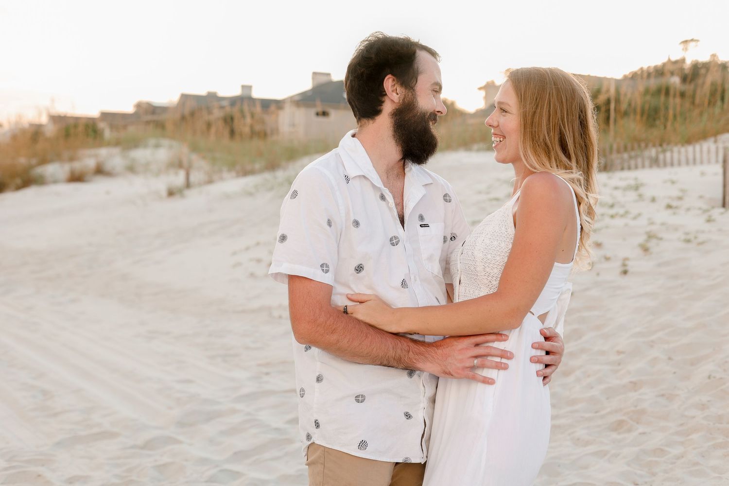 A couple embraces on a sandy beach during golden hour.