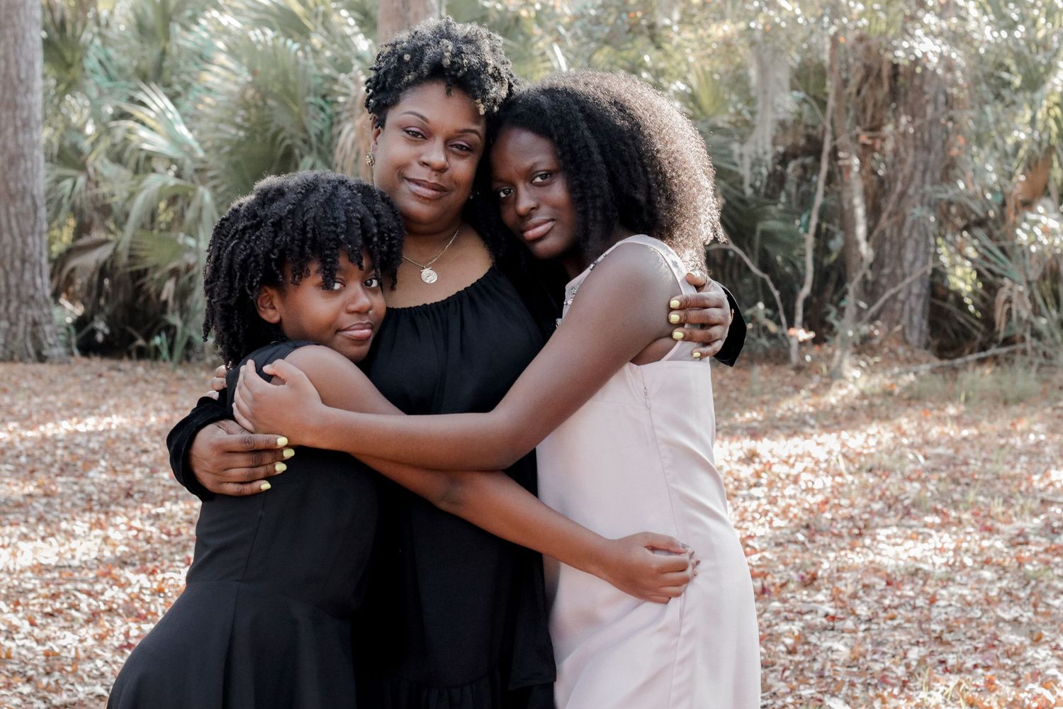 Three people share a warm embrace while standing together outdoors.