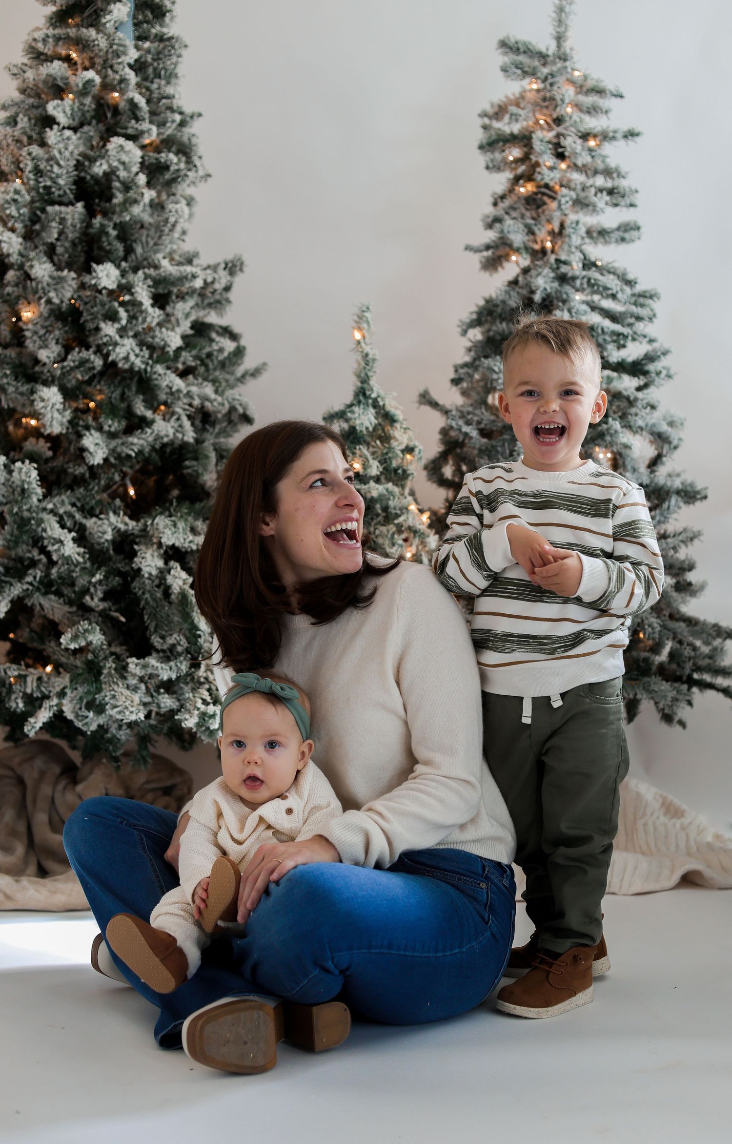 Candid family moment during Christmas photo session with flocked trees in background.