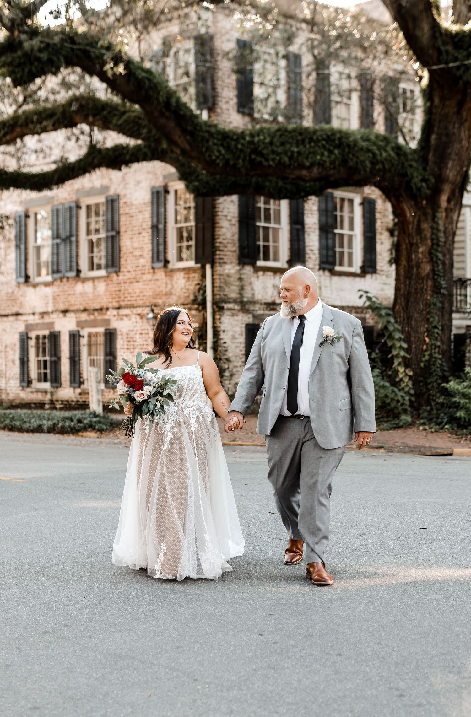 Wedding couple walking hand in hand outside historic ivy-covered brick building.