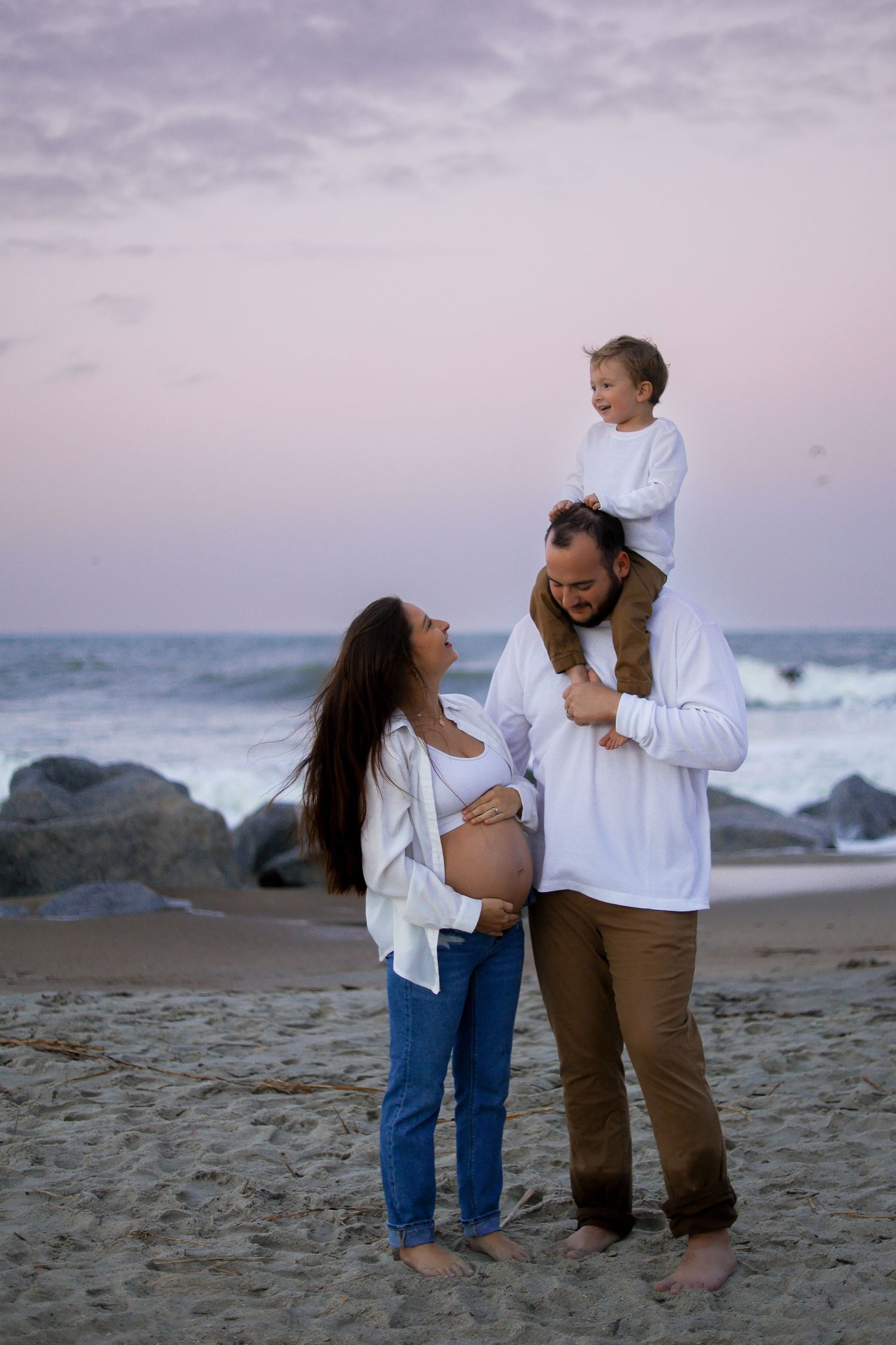 Couple sharing intimate moments on a rocky beach during purple sunset.