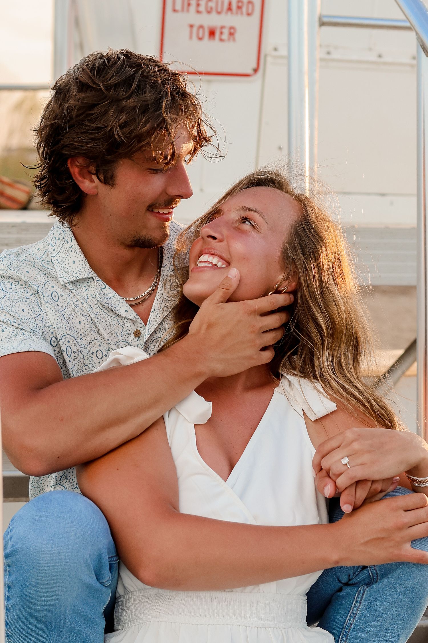 Couple sharing an affectionate moment while sitting on lifeguard tower steps.