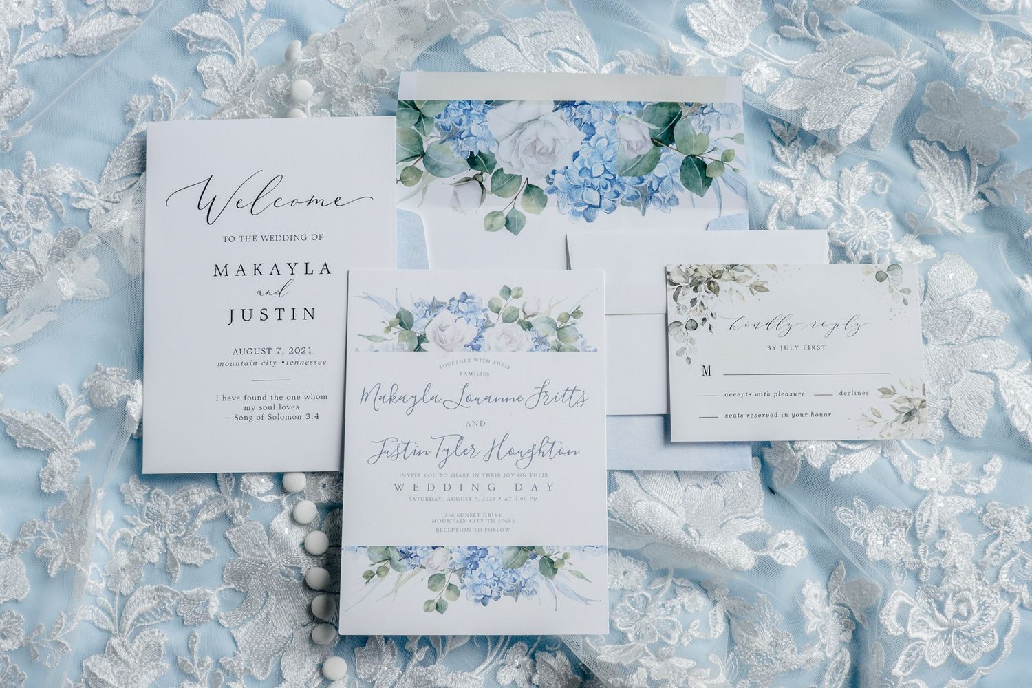 Delicate blue and white floral wedding invitation suite with elegant calligraphy on light background.