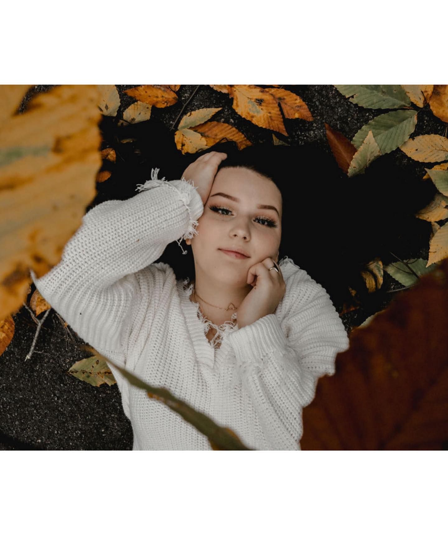 Autumn-themed portrait with white sweater against fallen orange leaves.