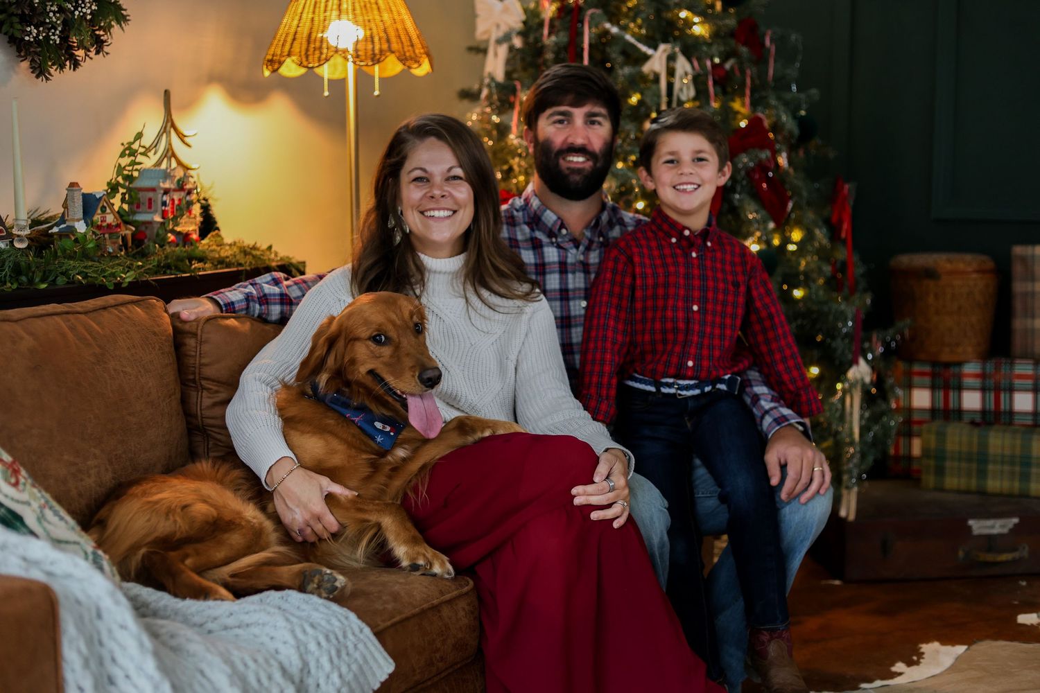 A family poses together on a couch with their brown dog during a cozy Christmas photoshoot at home.