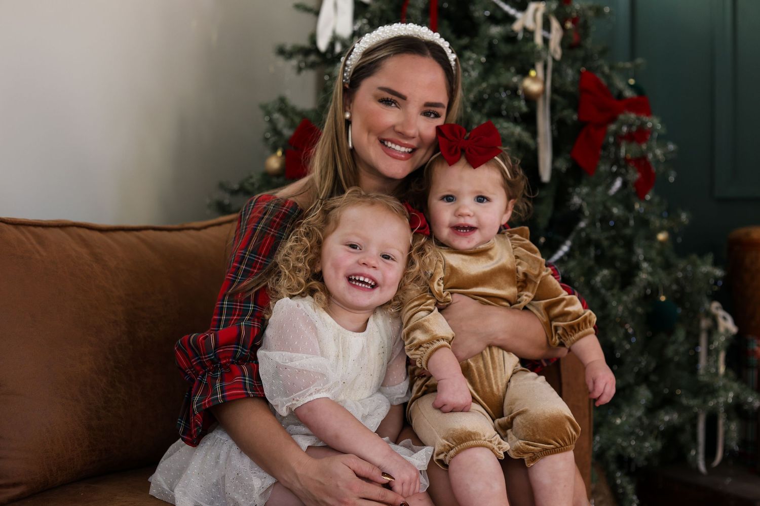 A festive holiday portrait on a brown couch with a decorated Christmas tree in the background.