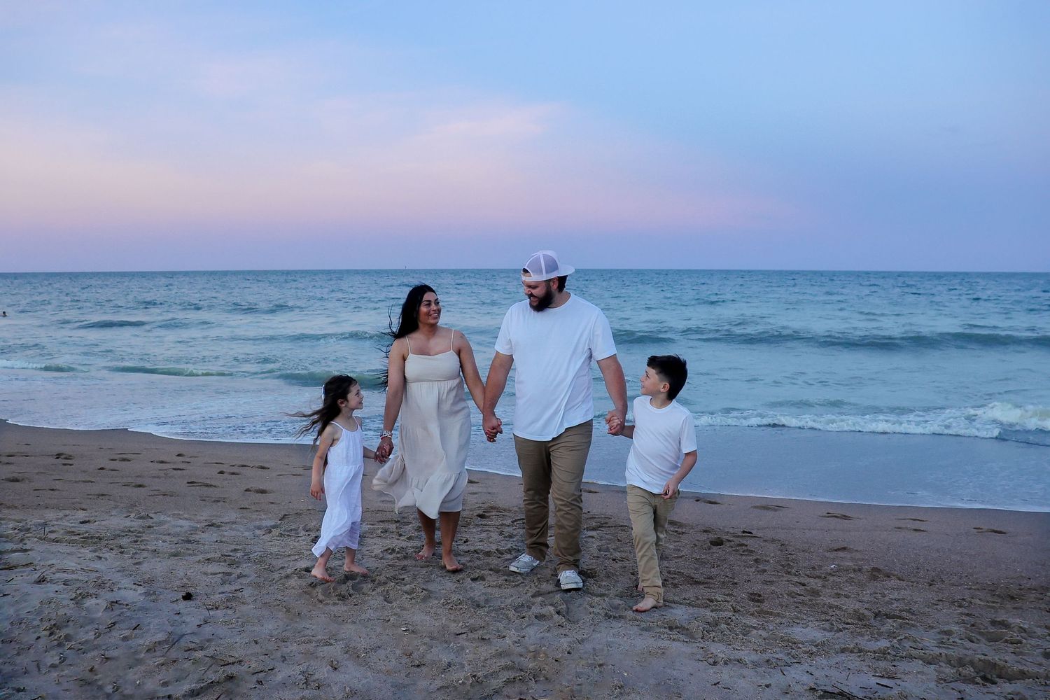 A family walks along a peaceful beach at sunset with ocean waves in the background.