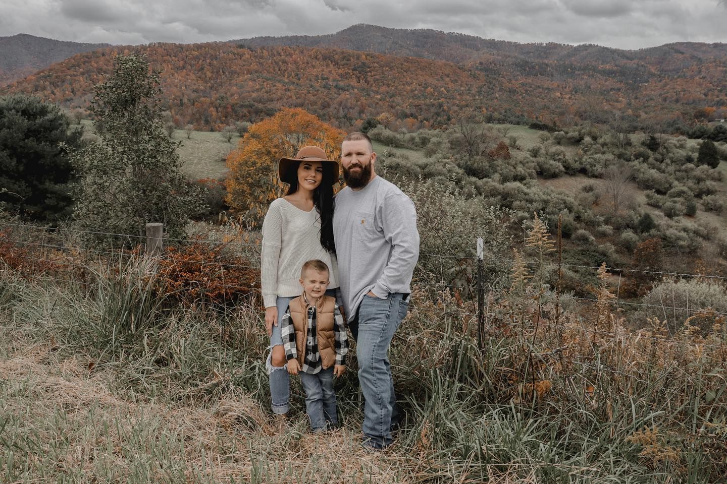 A couple stands together against a backdrop of autumn mountain scenery.
