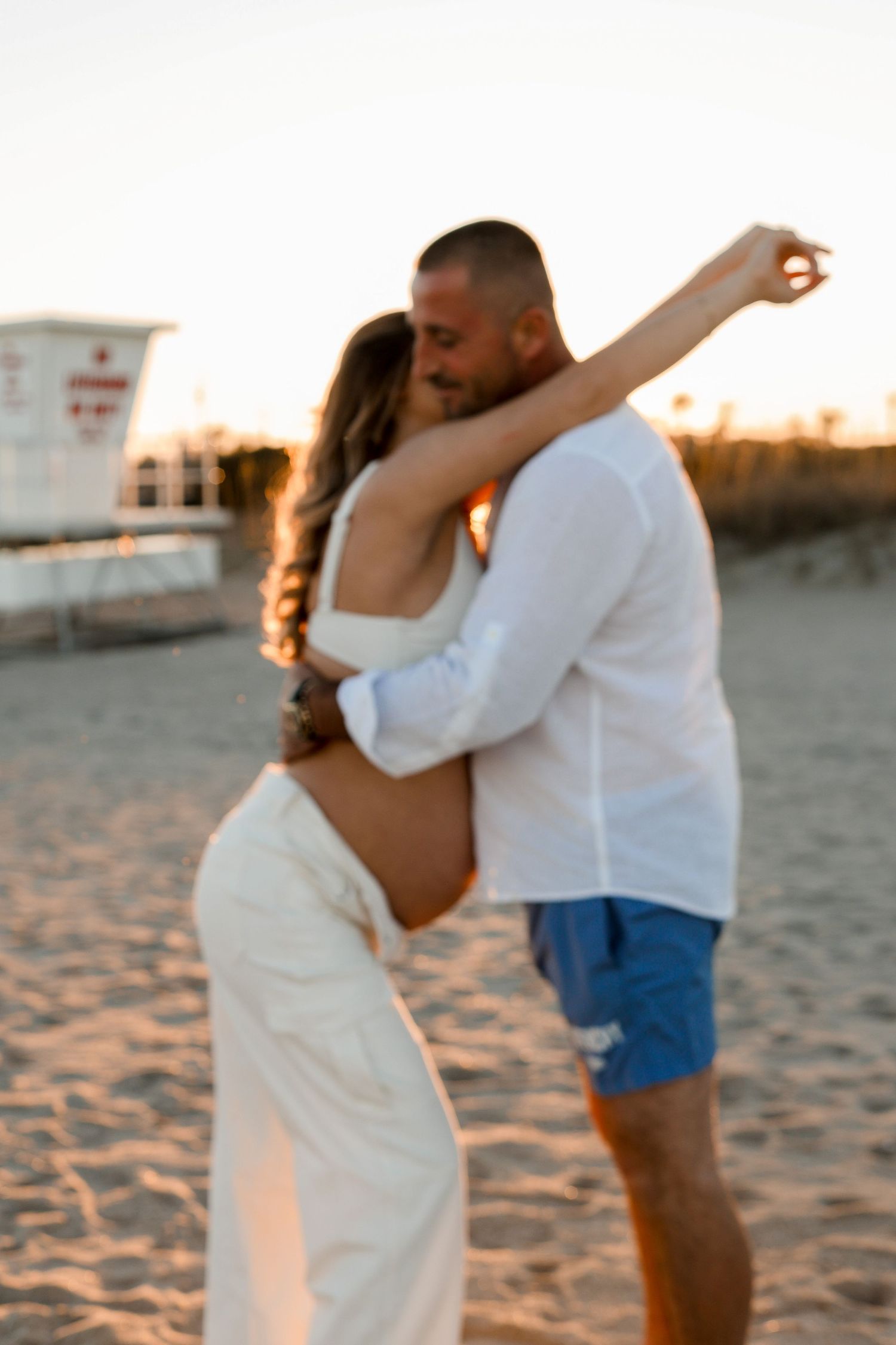 Couple dances joyfully on a sandy beach during sunset, celebrating a special moment.