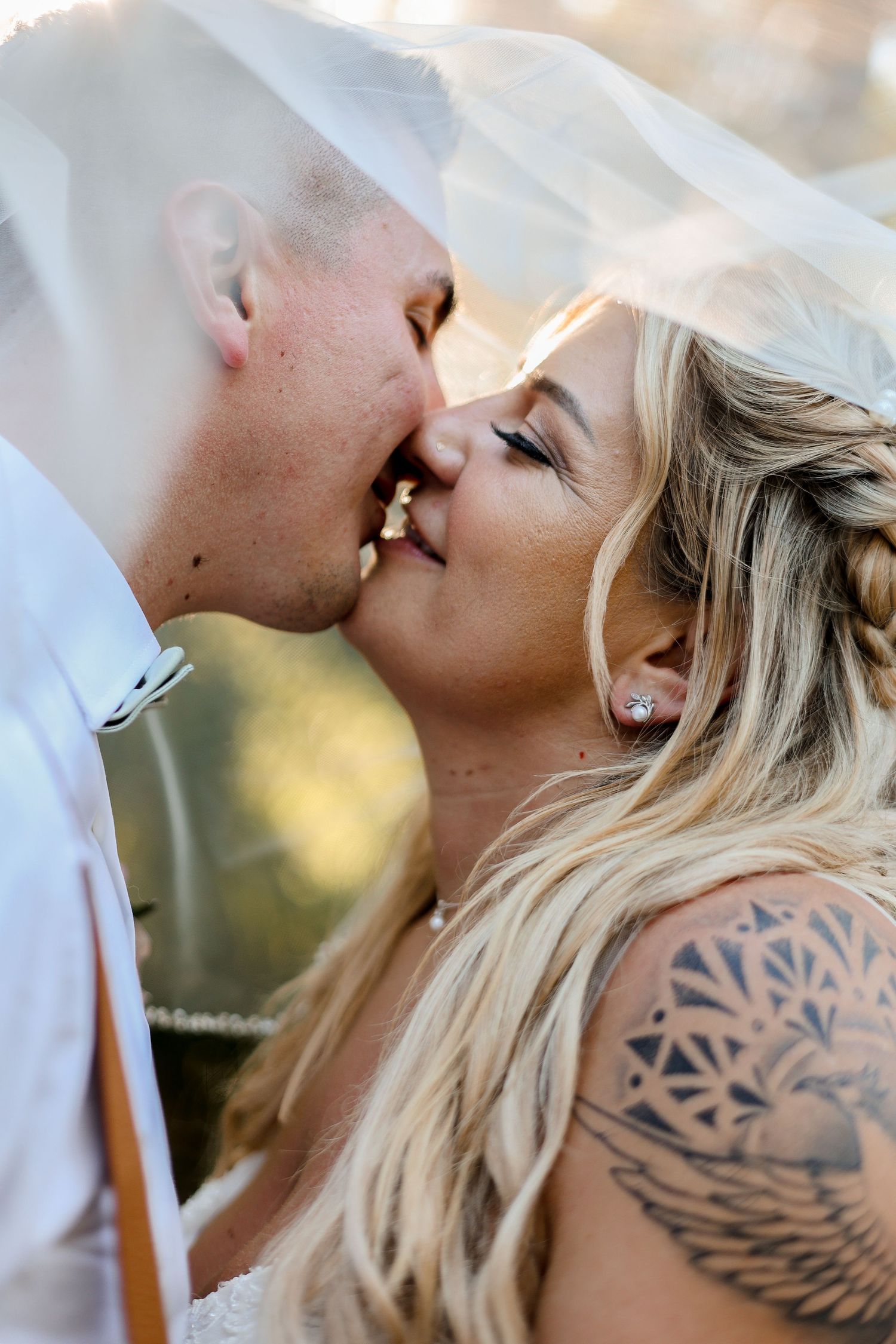 Close-up view showing two people kissing with a visible wing tattoo design.