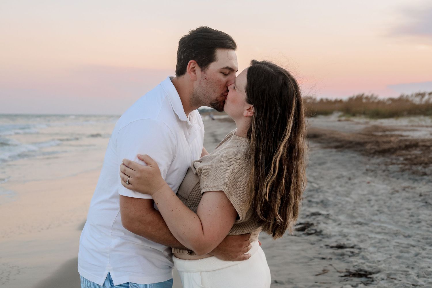 A couple shares romantic moments on a beach at sunset with the ocean in the background.