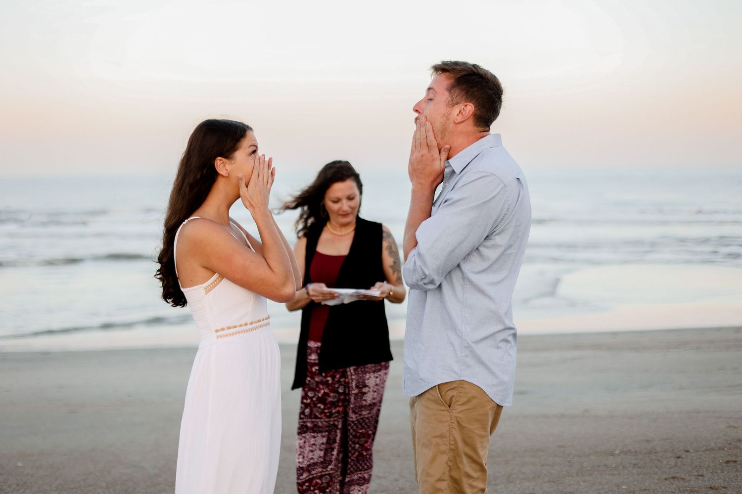 A beachside proposal ceremony with three people sharing a joyful moment.