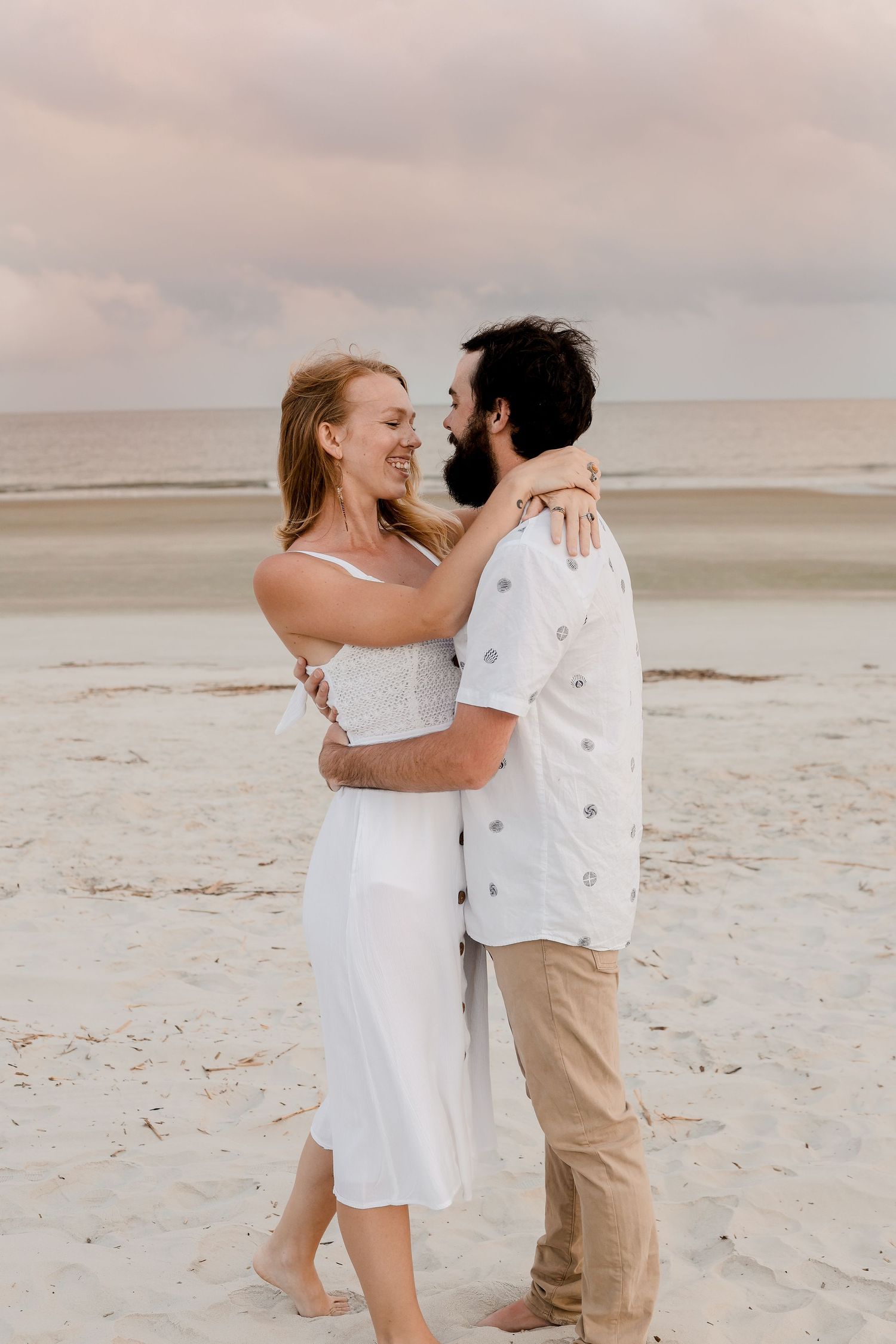 A couple embraces and dances playfully on a serene beach at sunset.