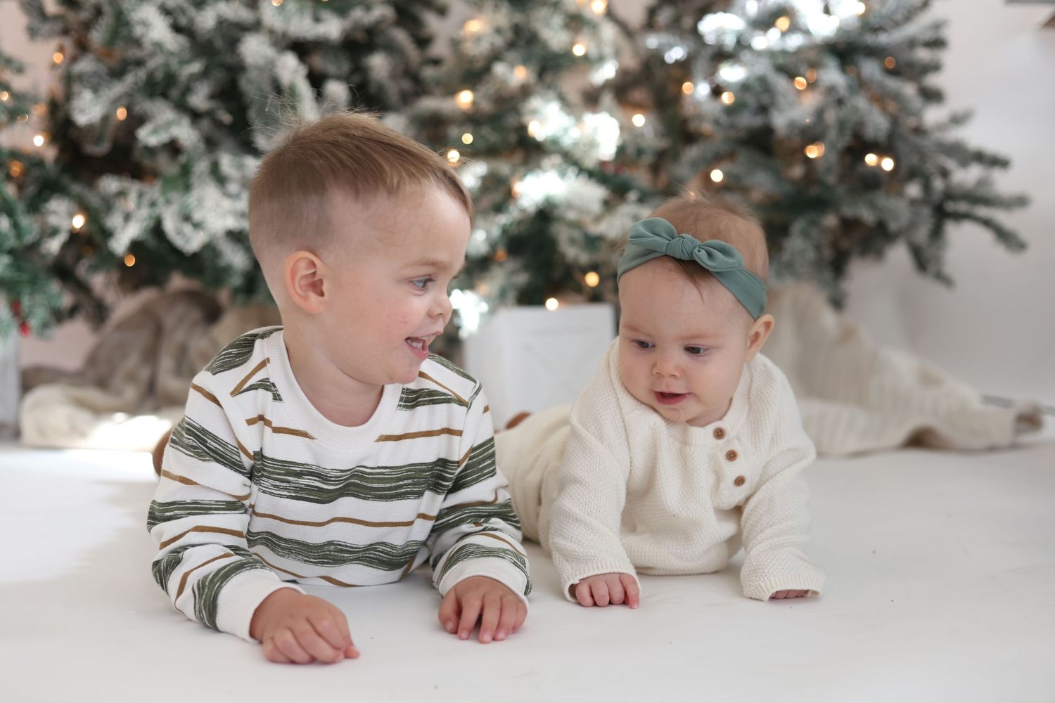 Siblings posing together during Christmas photo session with decorated trees.