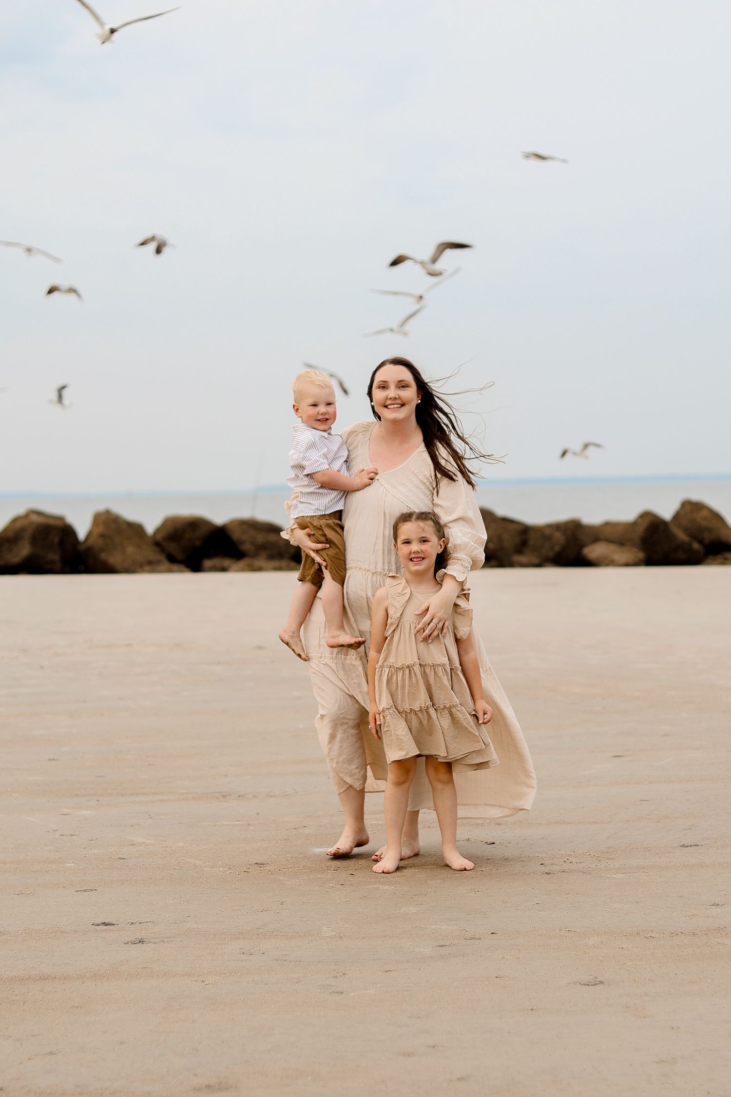 People stand on beach with seagulls flying overhead during golden hour.