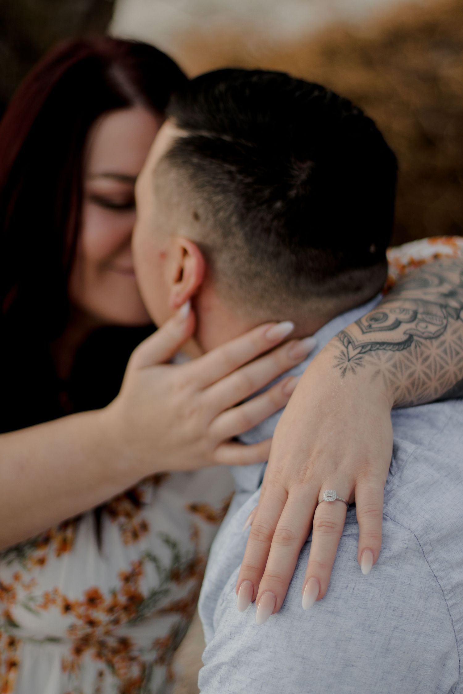 Intimate embrace showing engagement ring and tattooed arm details.