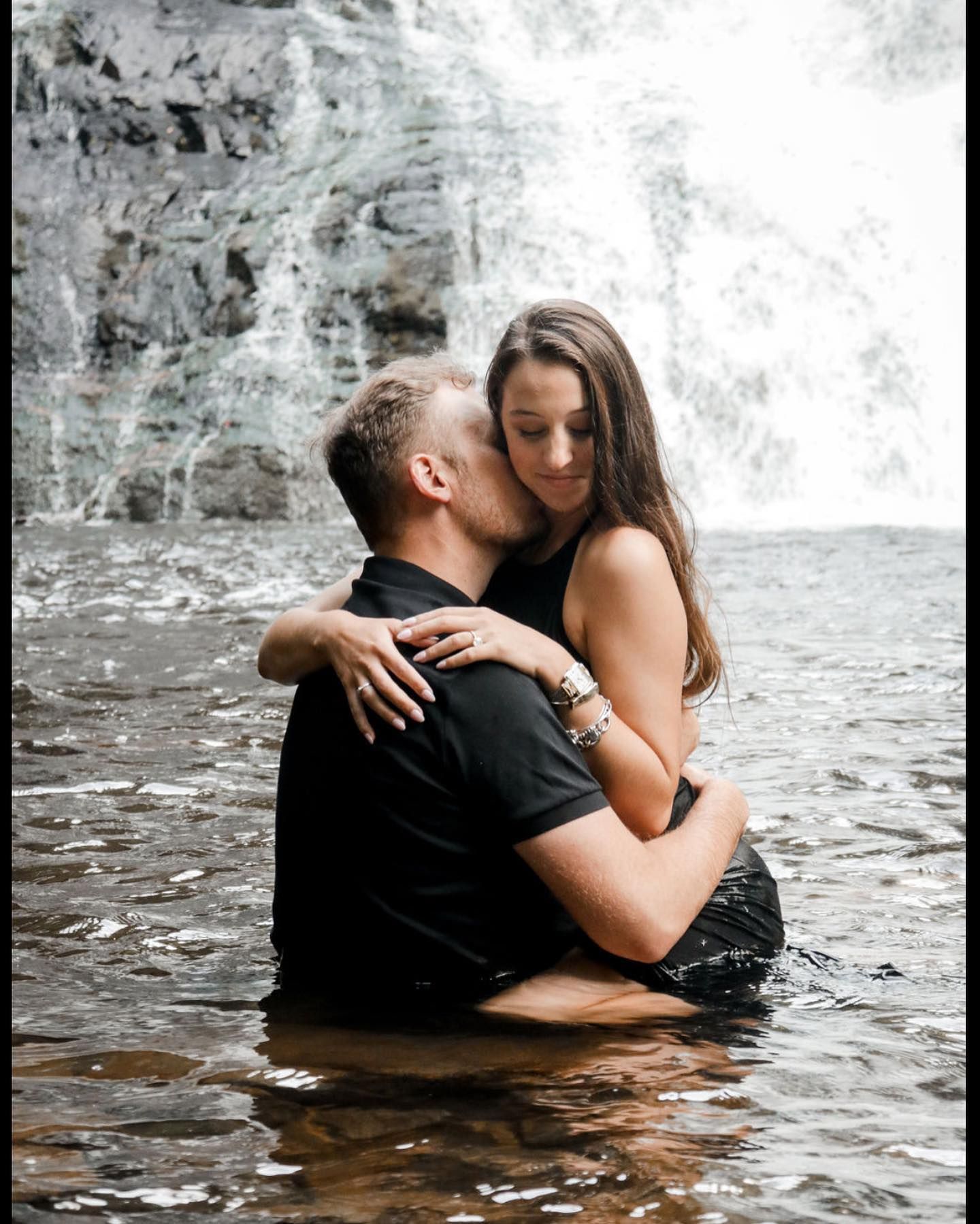 Romantic couple embracing in waterfall pool during intimate photoshoot.