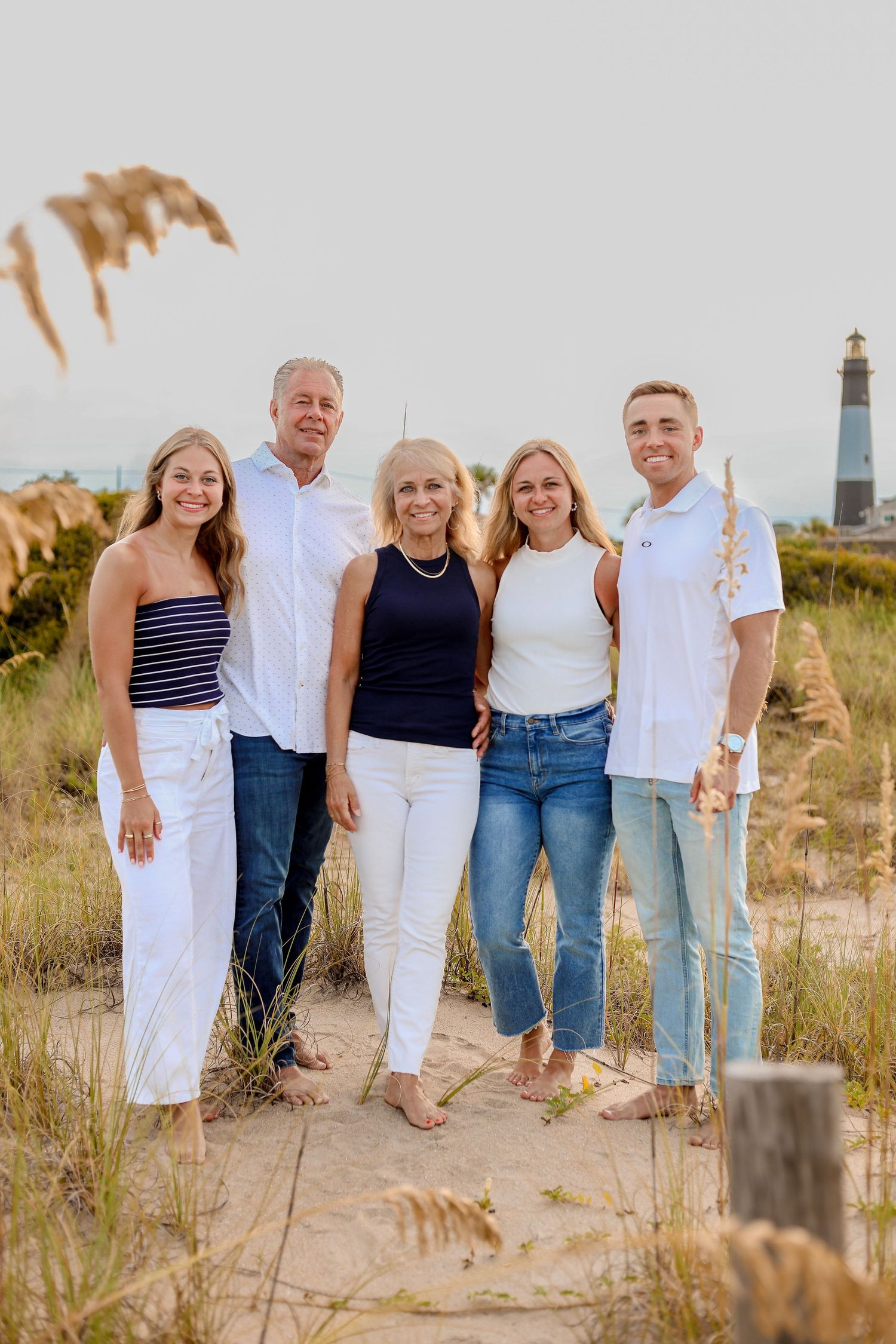 A group in coordinated white and blue outfits poses together on a sandy beach path during golden hour.