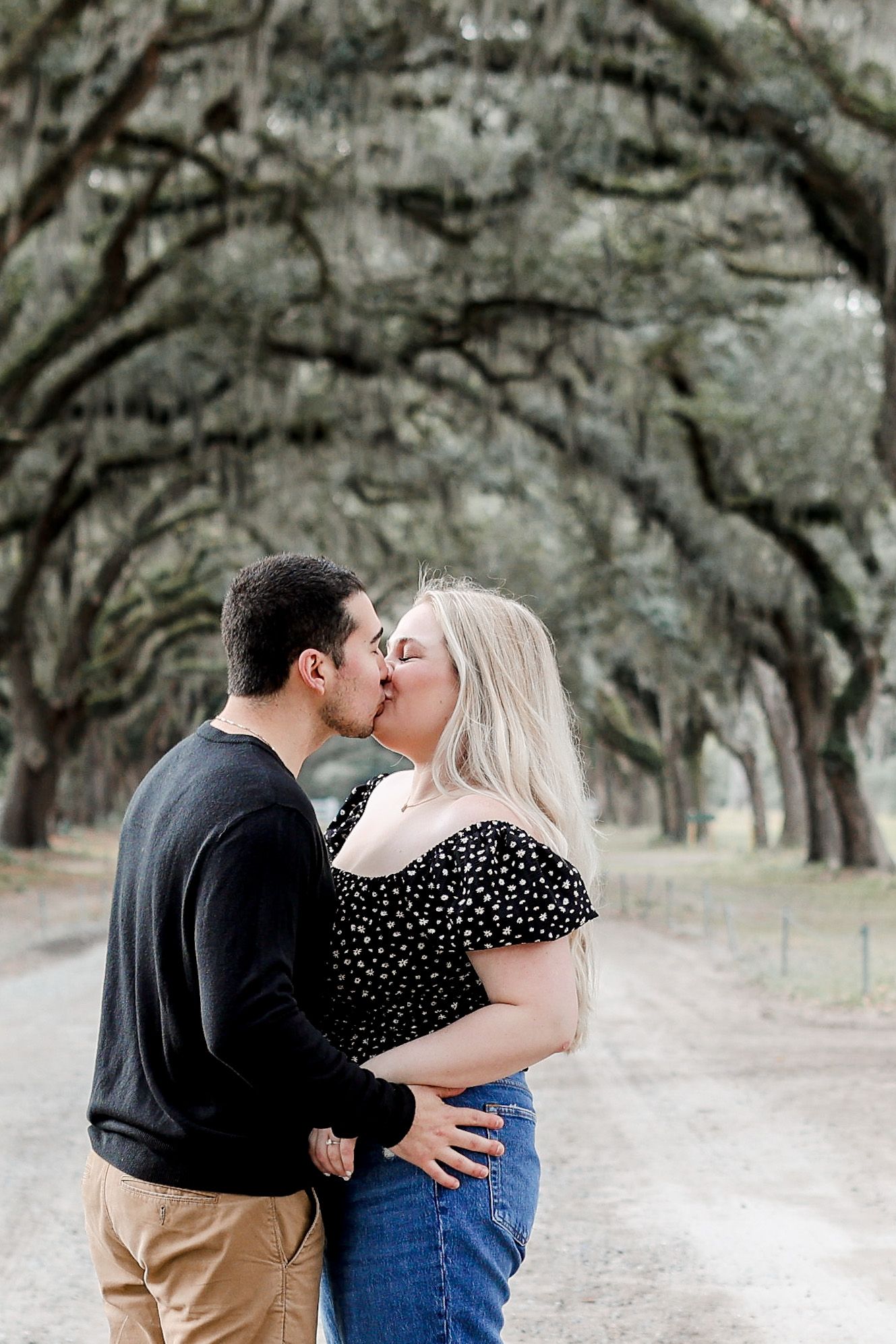 Intimate couple sharing a kiss under an archway of oak trees.