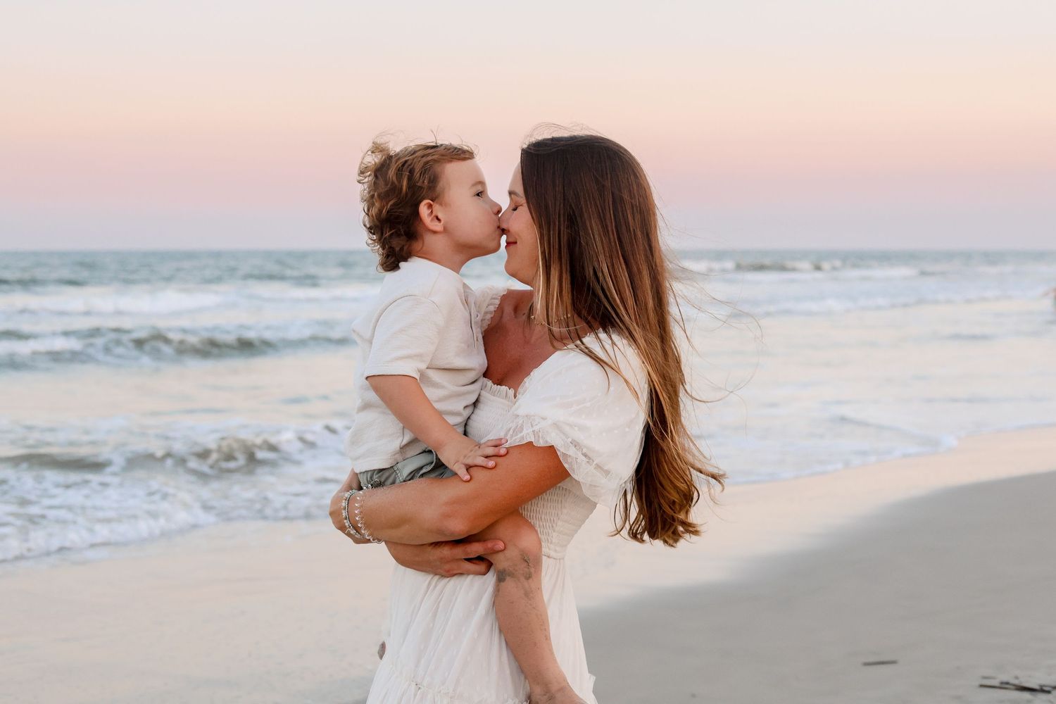 Family enjoying a playful moment together on sandy beach during golden hour with waves rolling in.