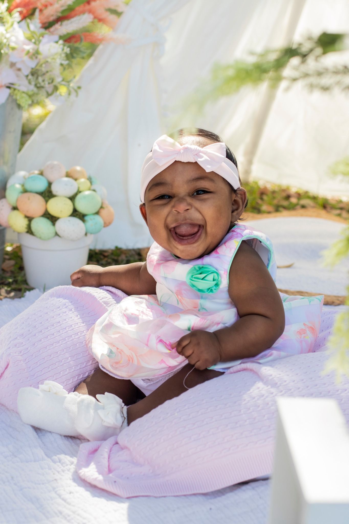 Baby resting on pink blanket with pastel balloons and decorative backdrop.