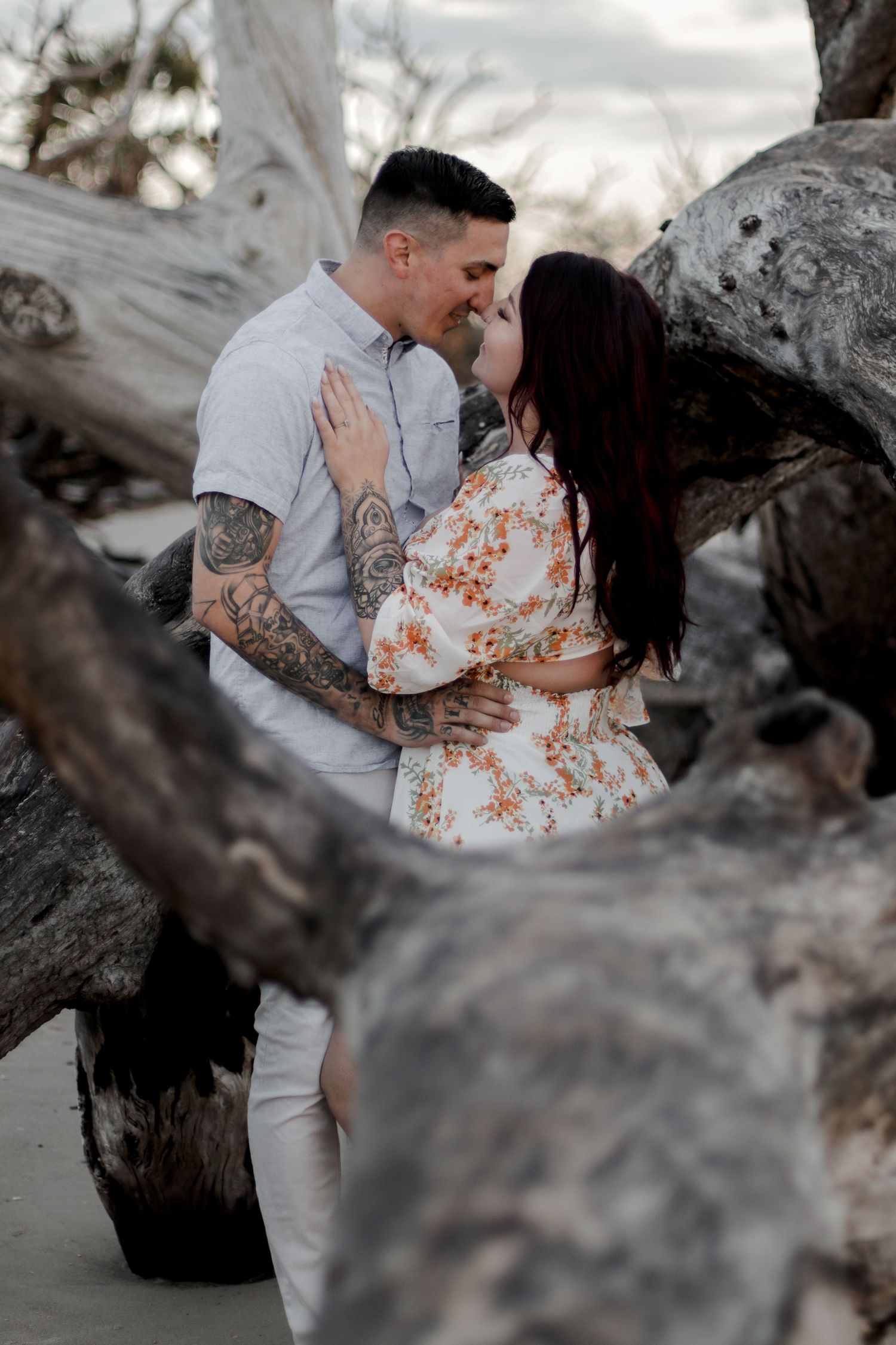 Romantic couple embracing among driftwood on a beach at dusk.