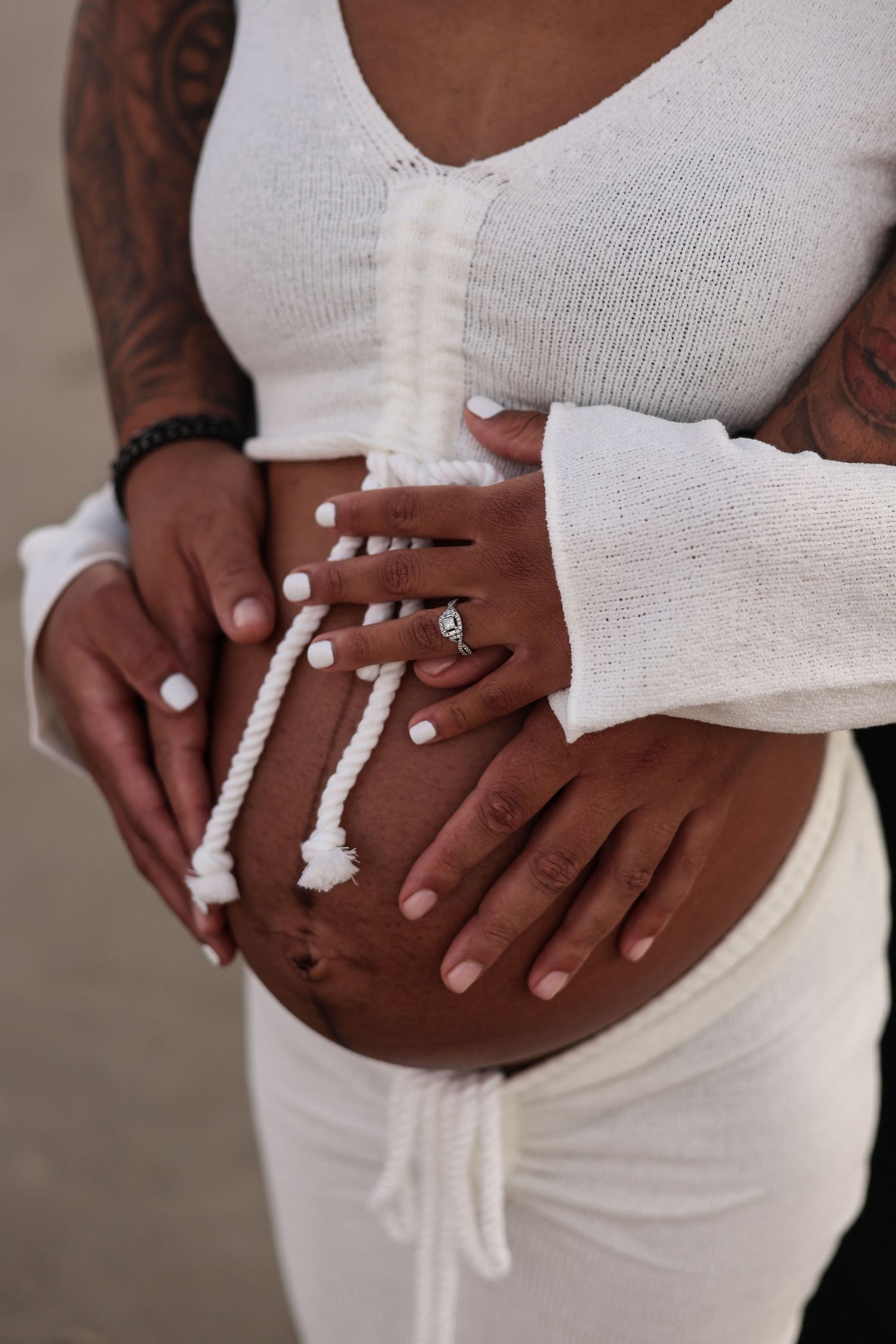 Close up of pregnant belly wrapped in white fabric with hands gently resting on top showing engagement ring.