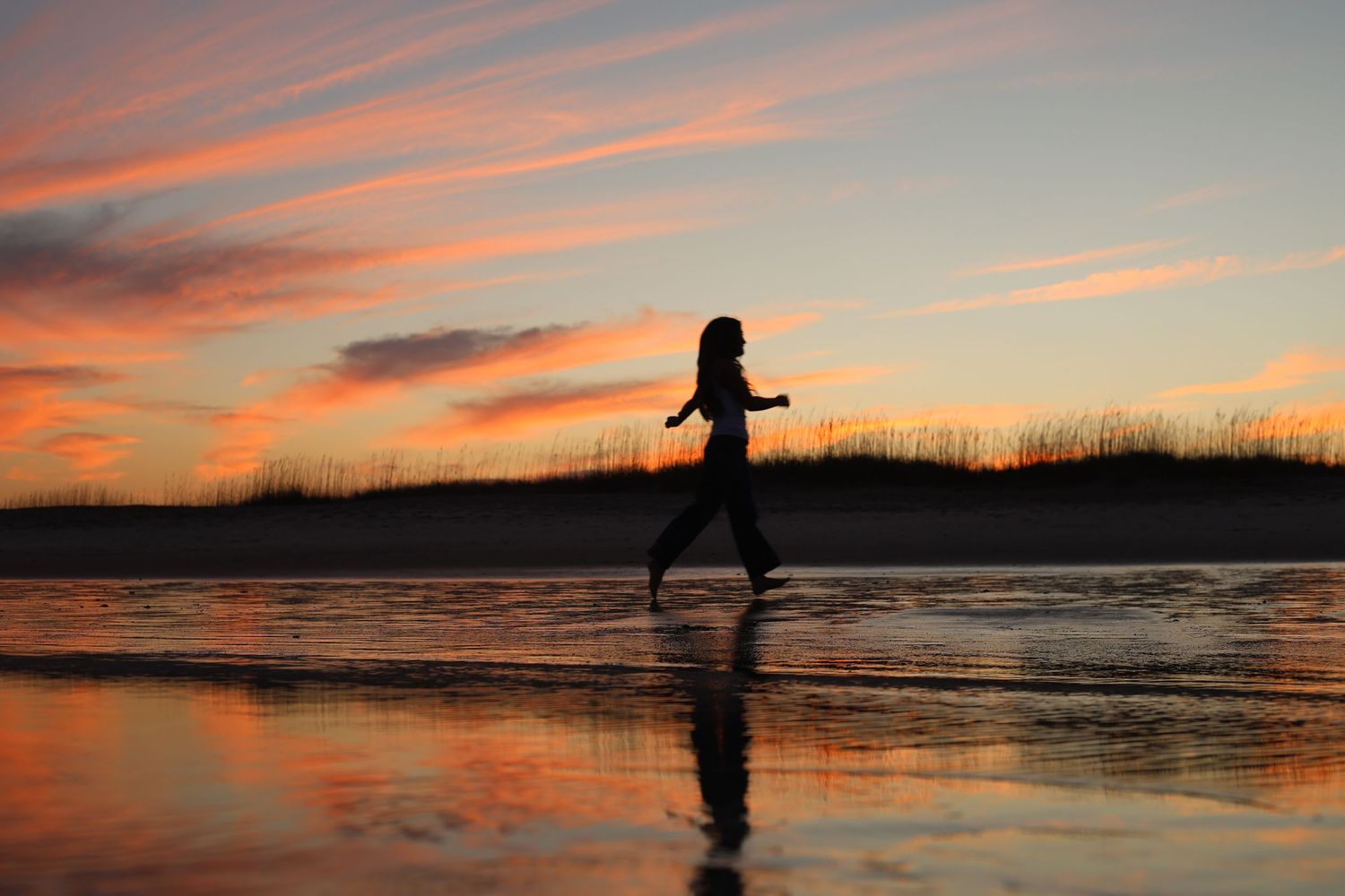 Silhouettes of a person against dramatic orange and pink sunset skies at the beach.