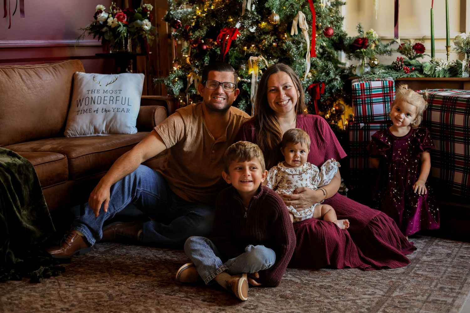 A smiling family of six poses together on a rug in front of a decorated Christmas tree in a cozy living room.