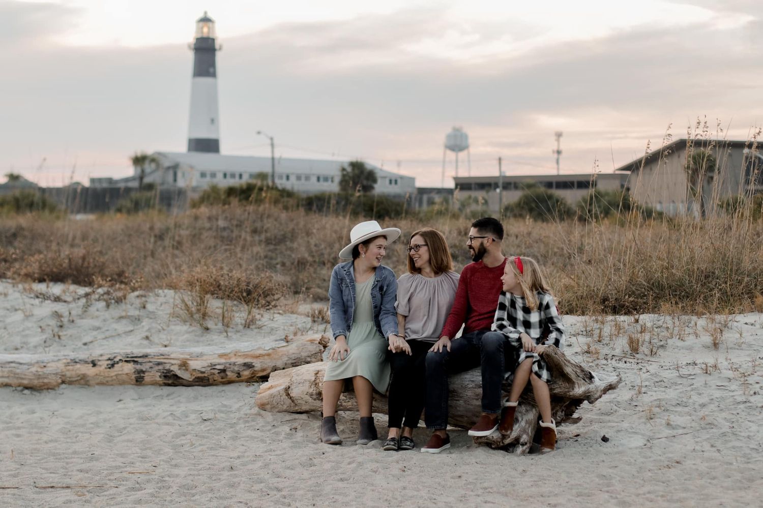 Scenic lighthouse beach photoshoot with people sitting in the sand at sunset.