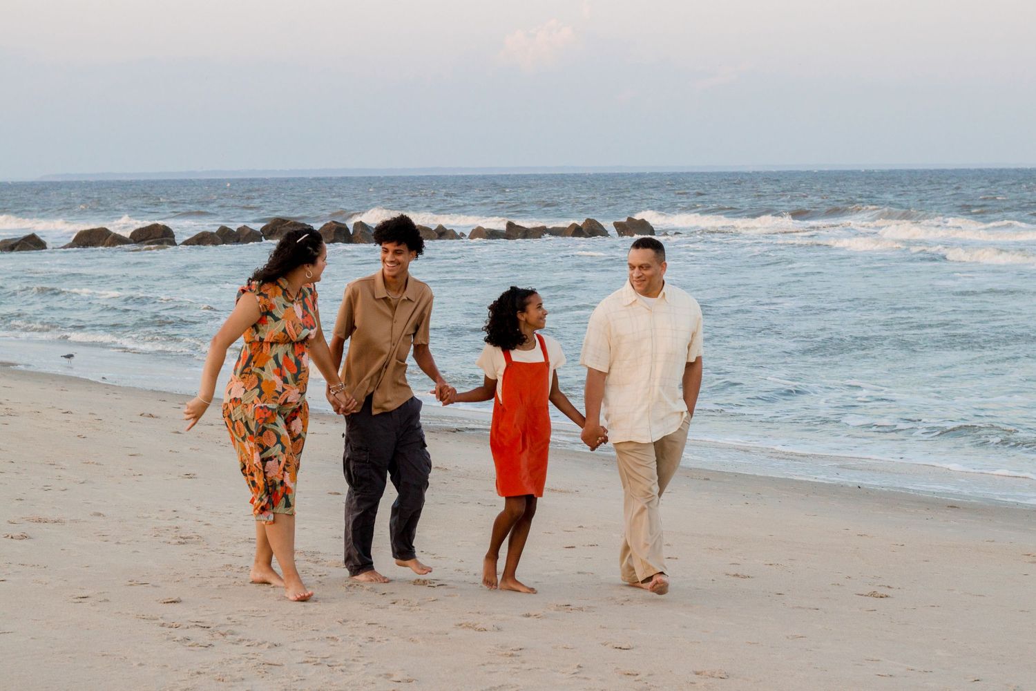 A group walks together along a sunny beach with waves crashing in the background.