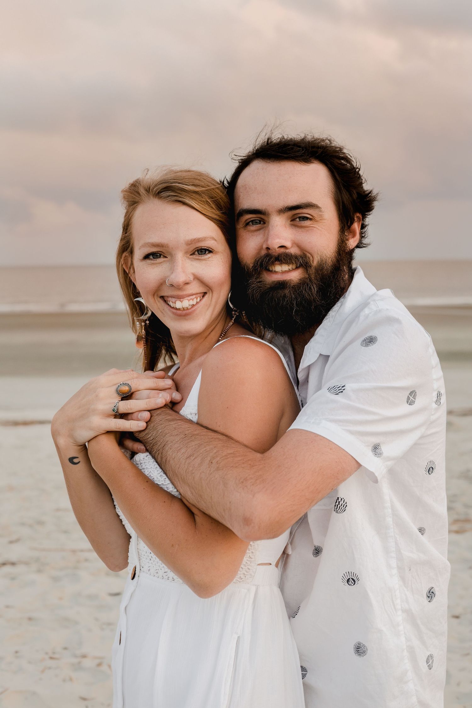 A couple shares intimate moments while posing for photos on a sandy beach.