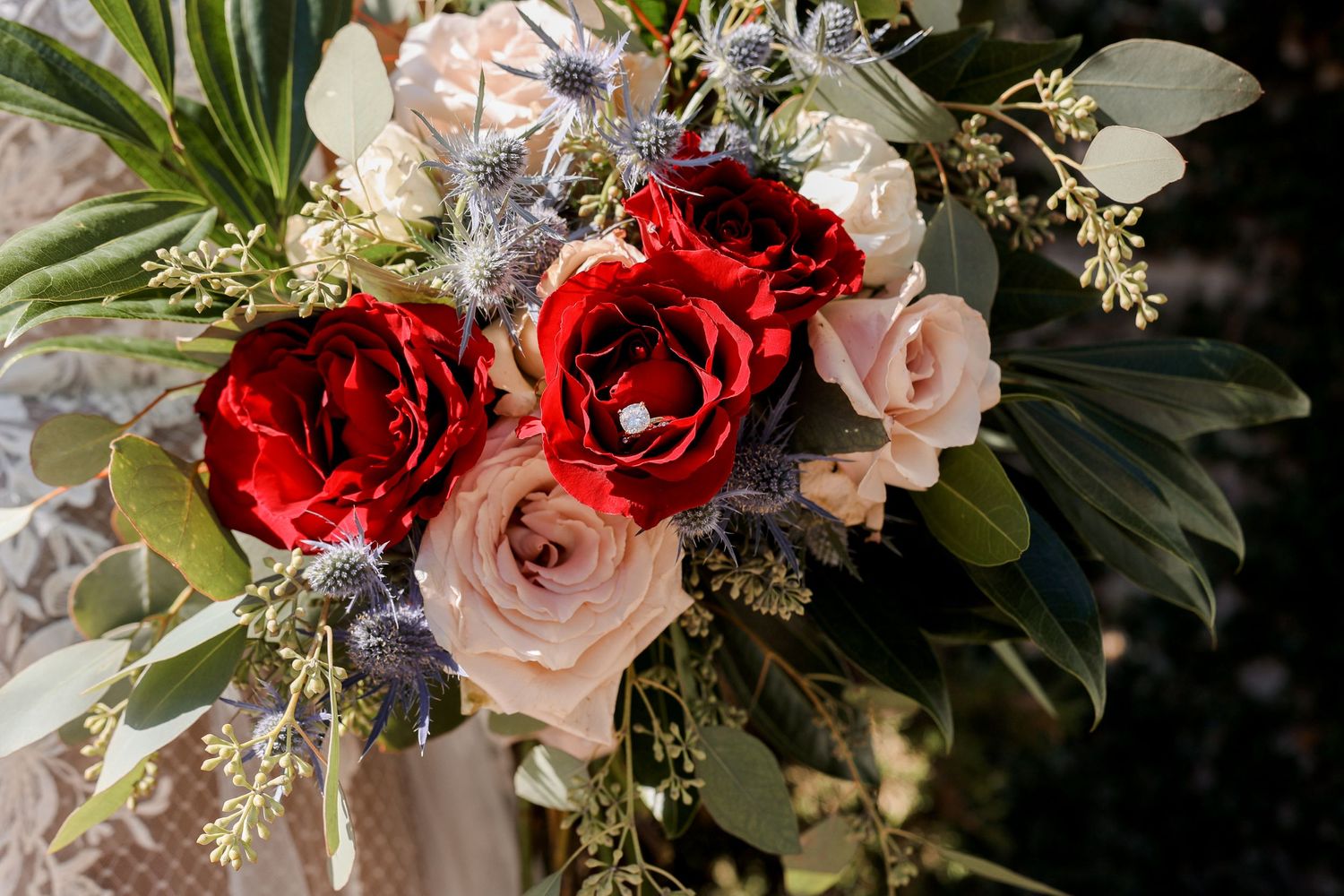 Wedding bouquet featuring deep red roses with blush pink flowers and greenery.