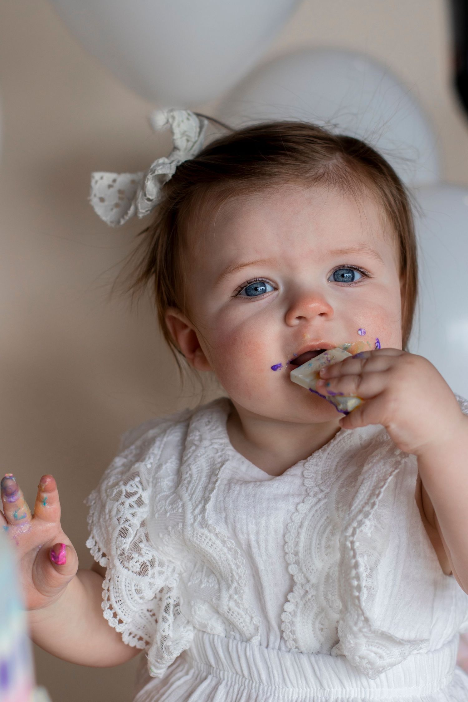 Baby in white lace dress smiling and playing with cake frosting during a smash cake photoshoot.